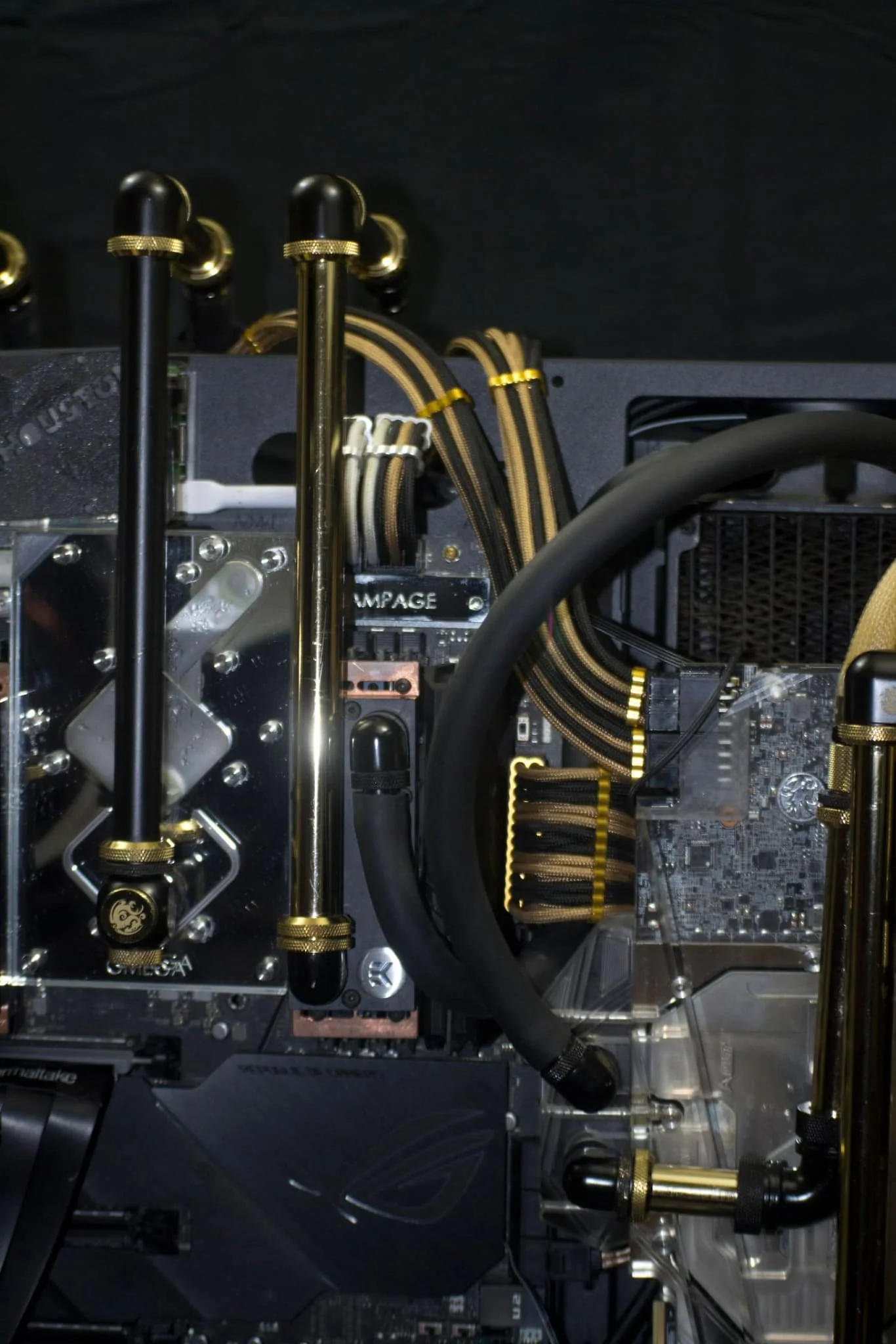 Close-up of a custom computer water cooling setup with black and gold accents, including reservoirs, tubing, and a transparent case showing internal components.