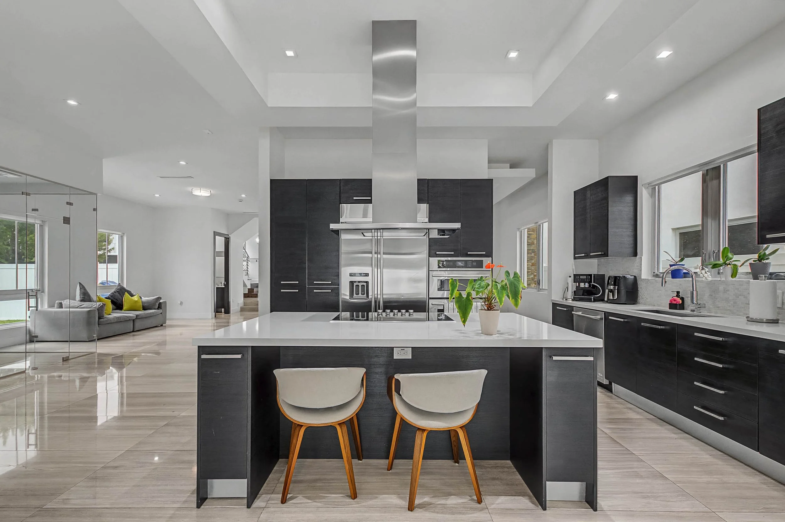Modern kitchen with black cabinets, stainless steel appliances, white countertops, and a central island with two chairs.
