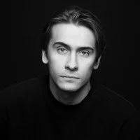 Black and white portrait of a young man with dark hair and a serious expression.