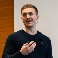 Young man speaking and gesturing with his hand in an indoor setting.