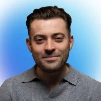 Portrait of a man with short dark hair and a slight smile, against a blue background.