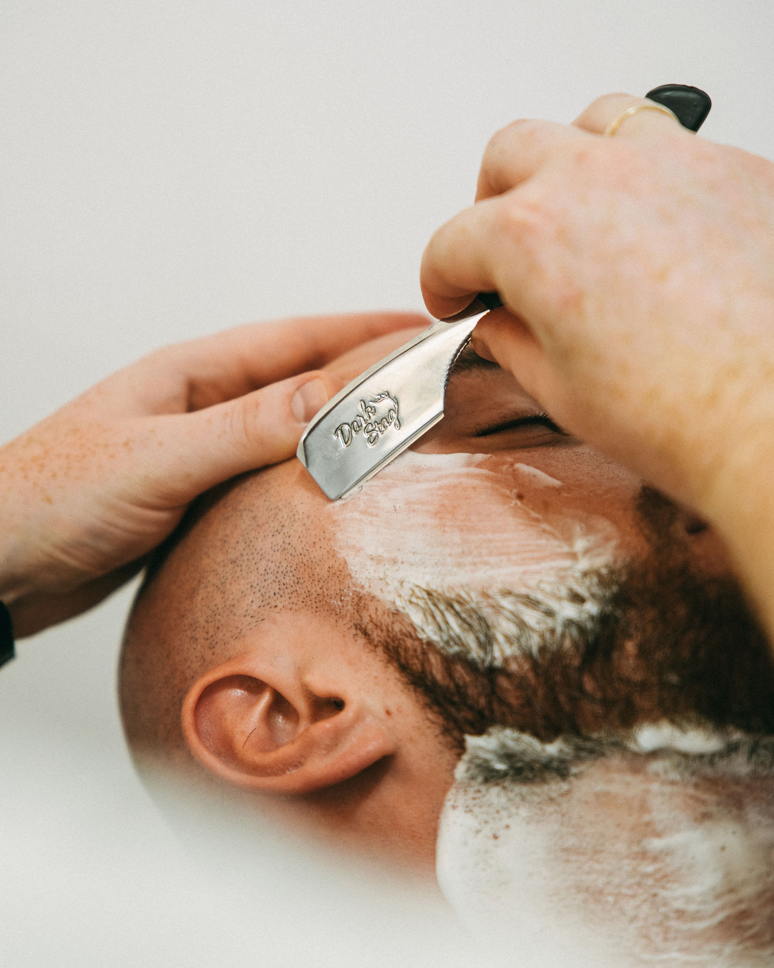 Close-up of a person receiving a facial massage with a steel tool engraved with "Double Snap" on the forehead, and their face covered in a white cream.