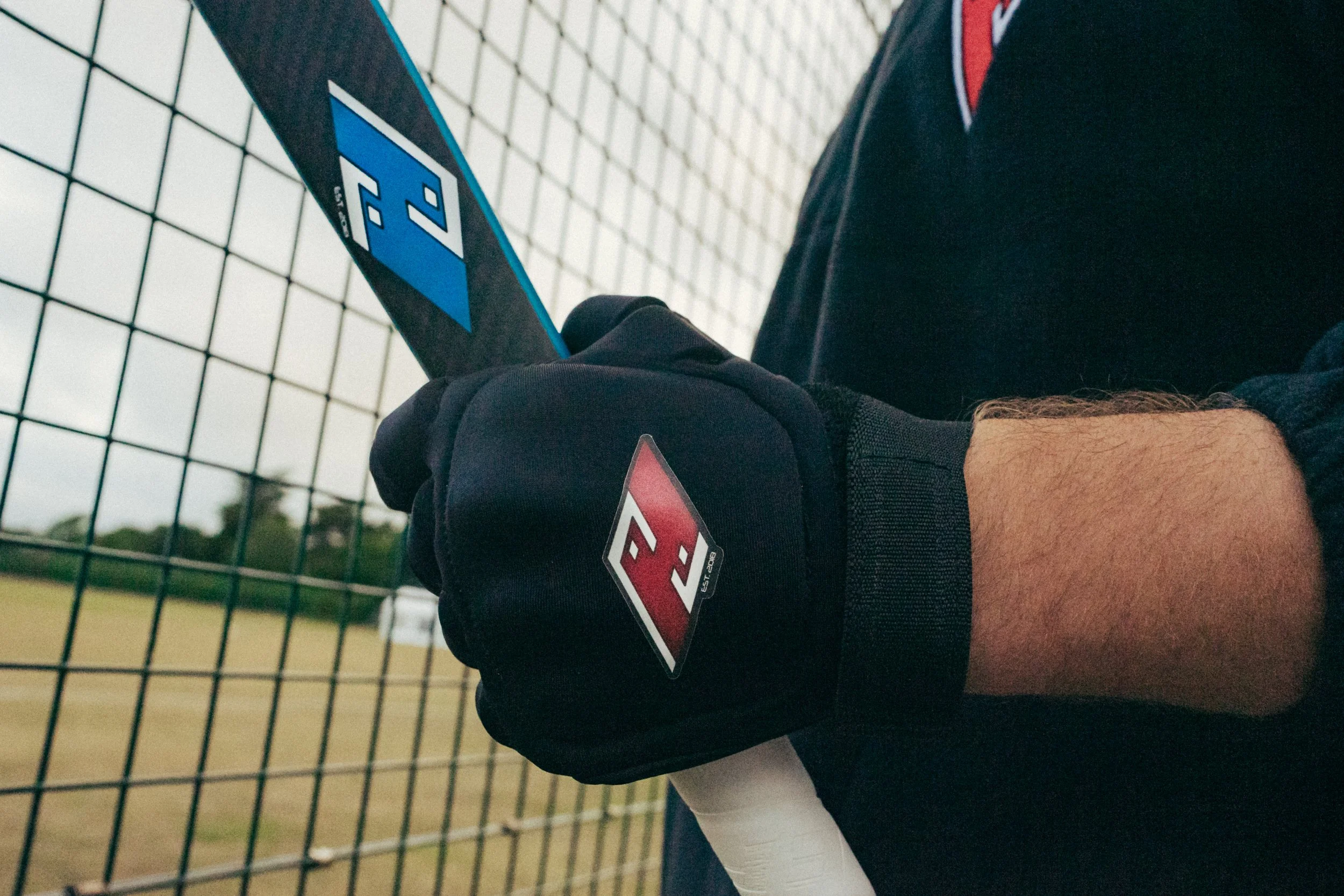 Close-up of a person's hand wearing a black glove holding a blue and black tennis racket near a tennis net.