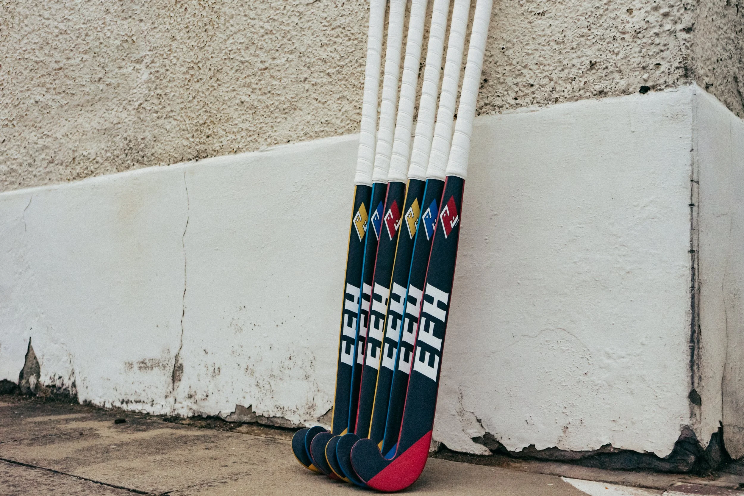 Five hockey sticks with blue, red, and black design leaning against a textured light-colored wall.