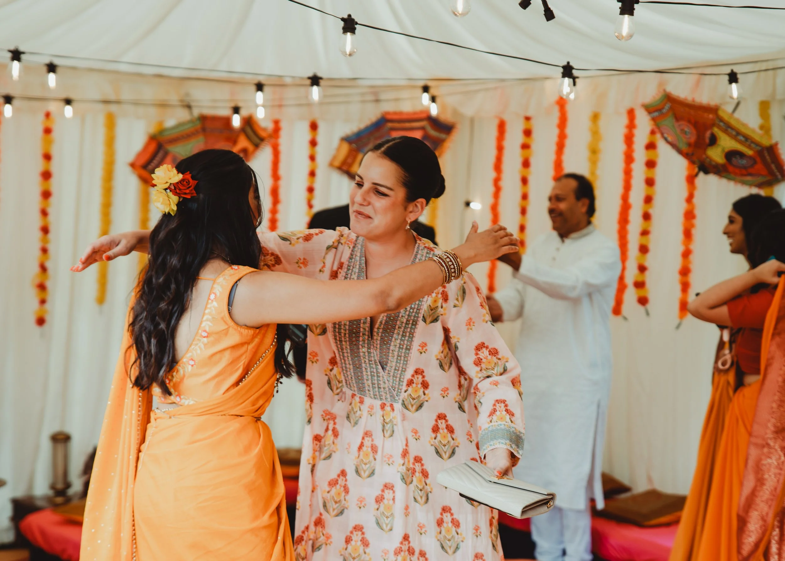 Women dancing and celebrating at a fiesta event decorated with marigold flowers, paper umbrellas, and string lights.