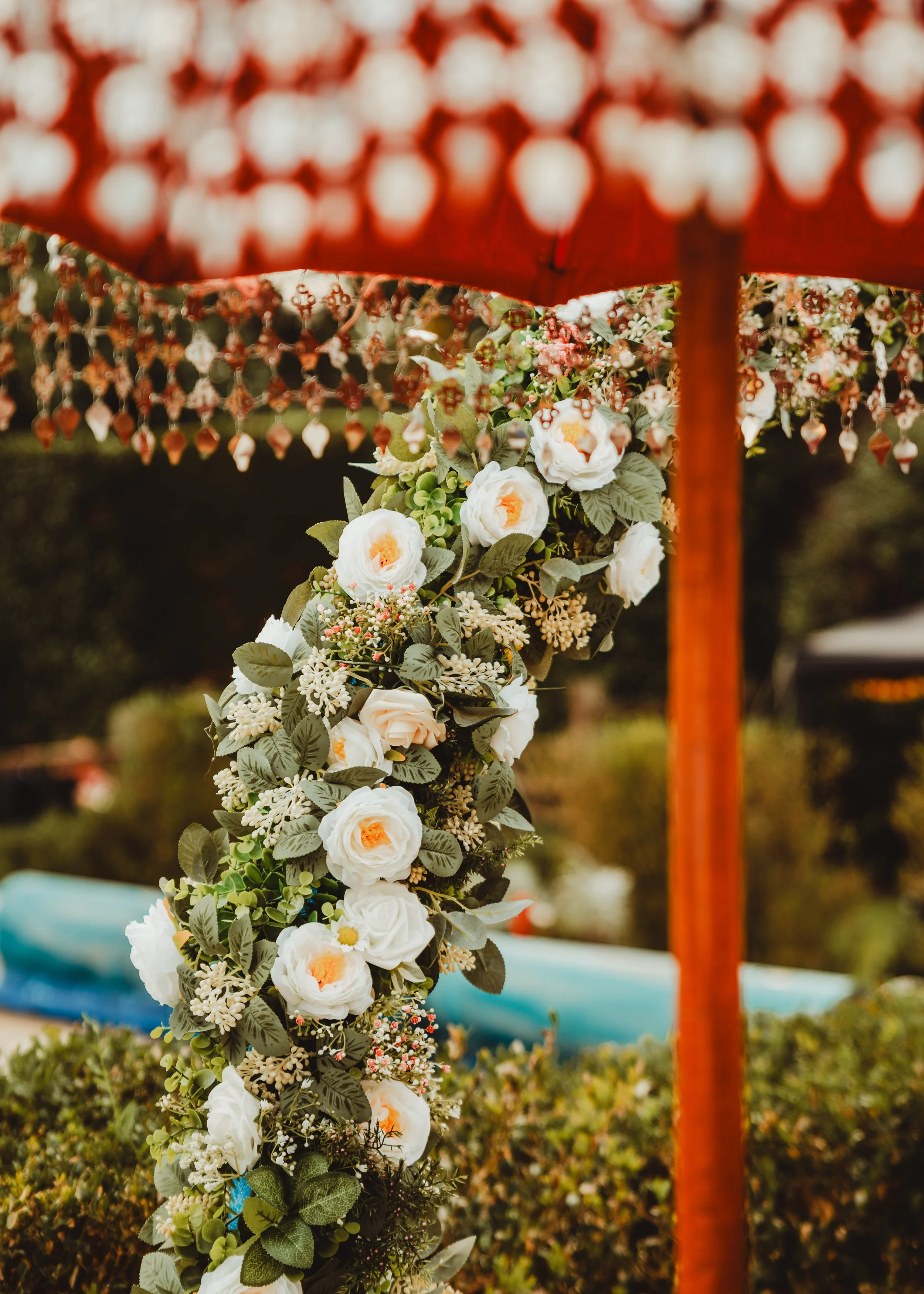 A floral wedding decoration featuring white roses, pink flowers, and green foliage, placed beneath a red chandelier with hanging crystals.