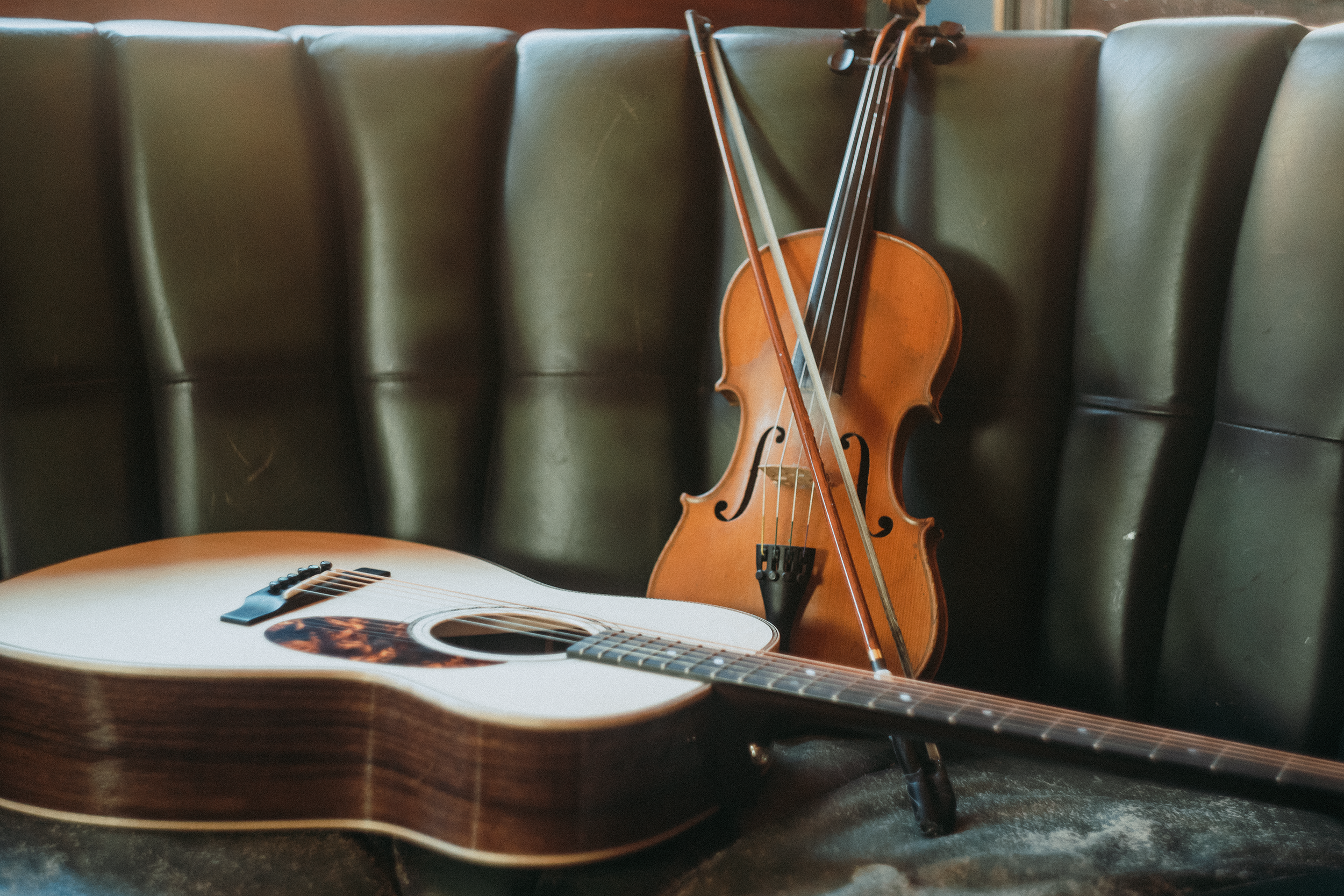 An acoustic guitar and a violin resting against a padded bench.