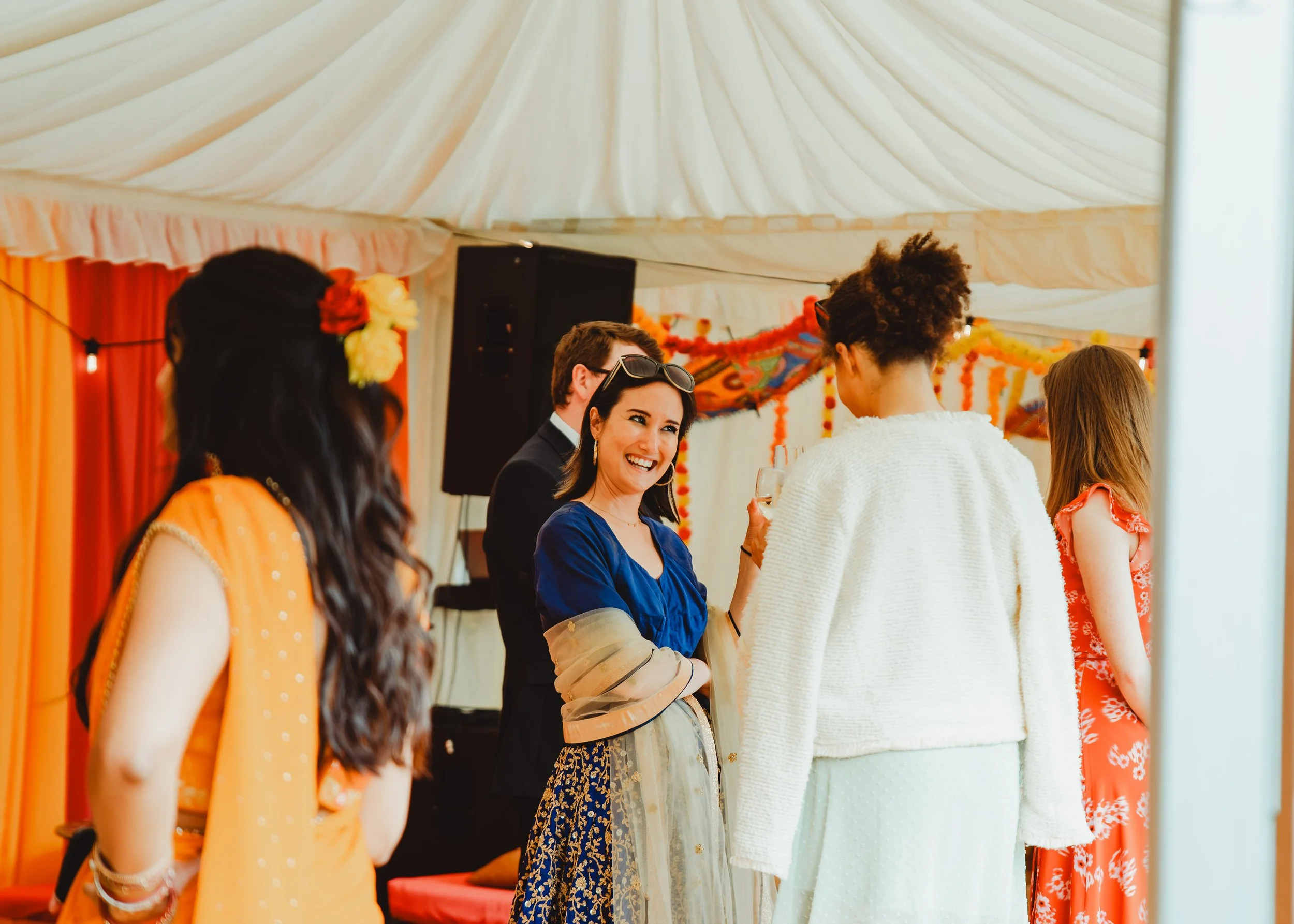 Group of diverse people socializing at a festive gathering under a decorated tent with orange and yellow accents.