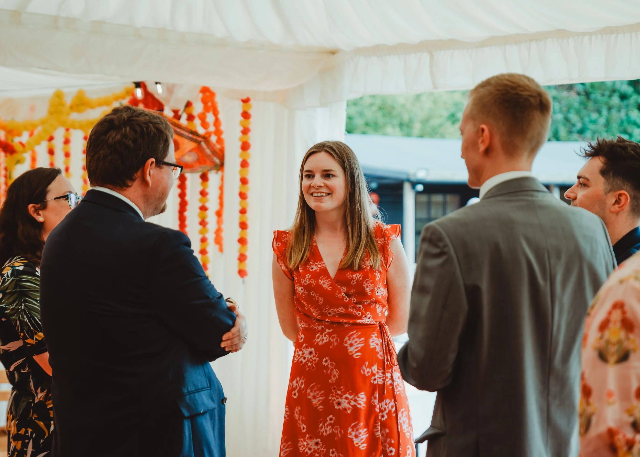 A group of people, including young adults and a woman, gathered in a decorated outdoor setting, exchanging greetings and smiles at a celebratory event.