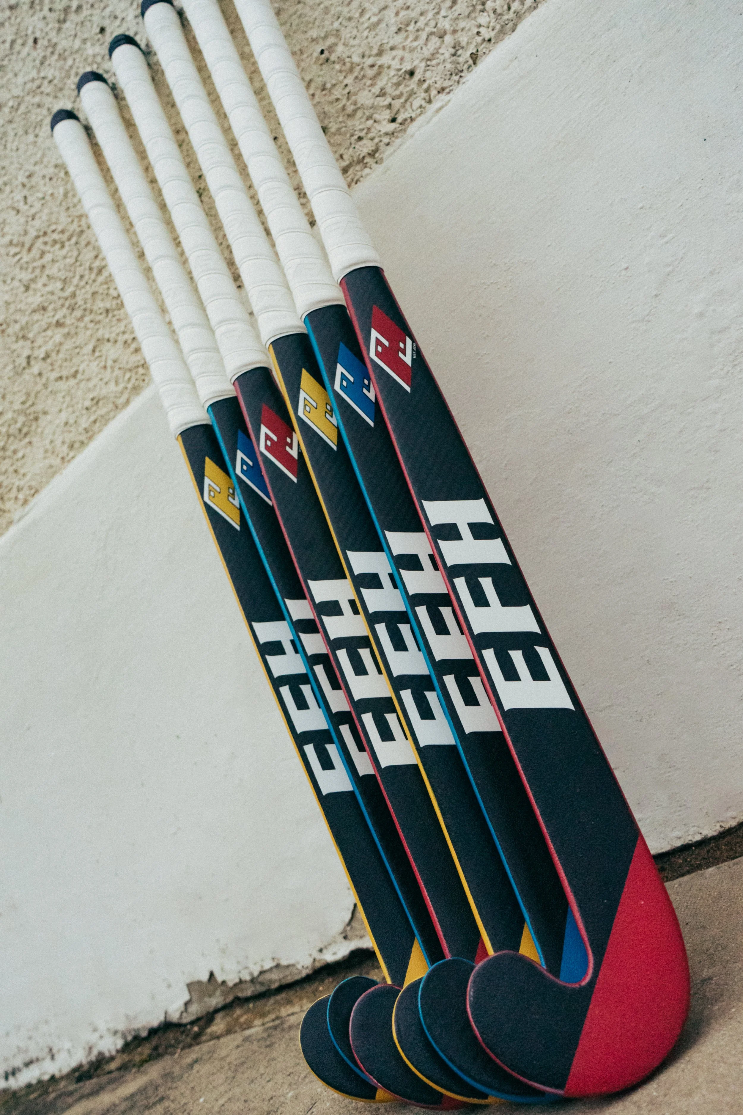 Set of colorful hockey sticks arranged against a wall with the blades on the floor.