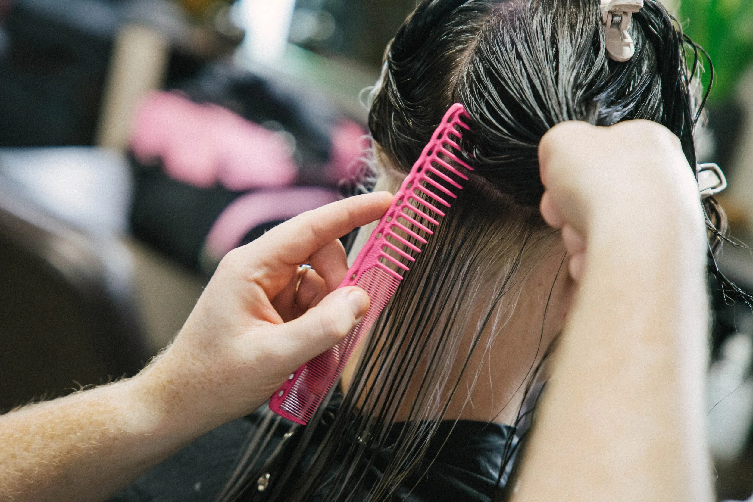 A person with dark, wet hair getting a haircut, with a pink comb used to detangle and style the hair.