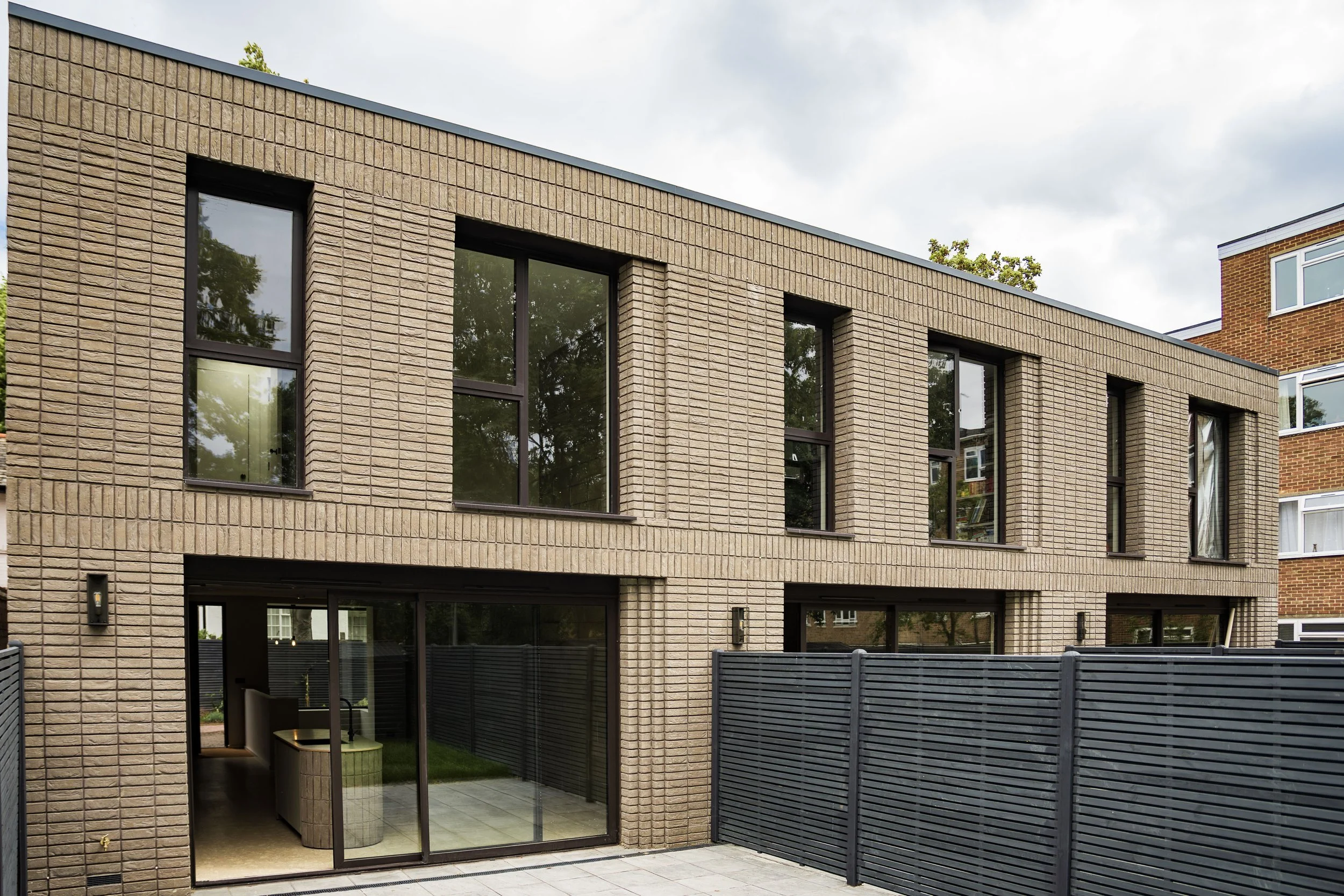 Modern beige brick building with large rectangular windows and a black fence in the backyard.