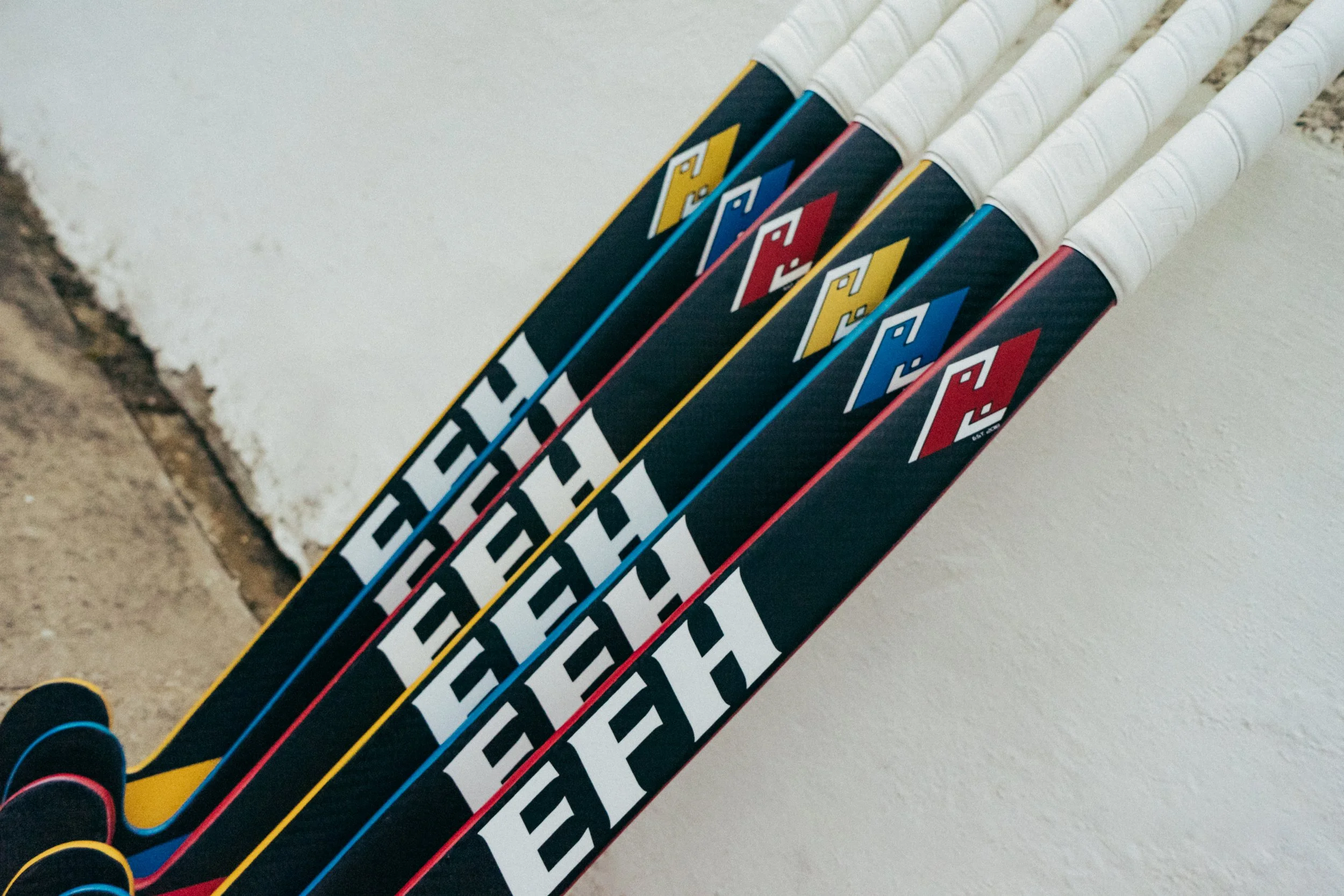 A row of colorful tennis rackets with black and white grips, leaning against a white wall.