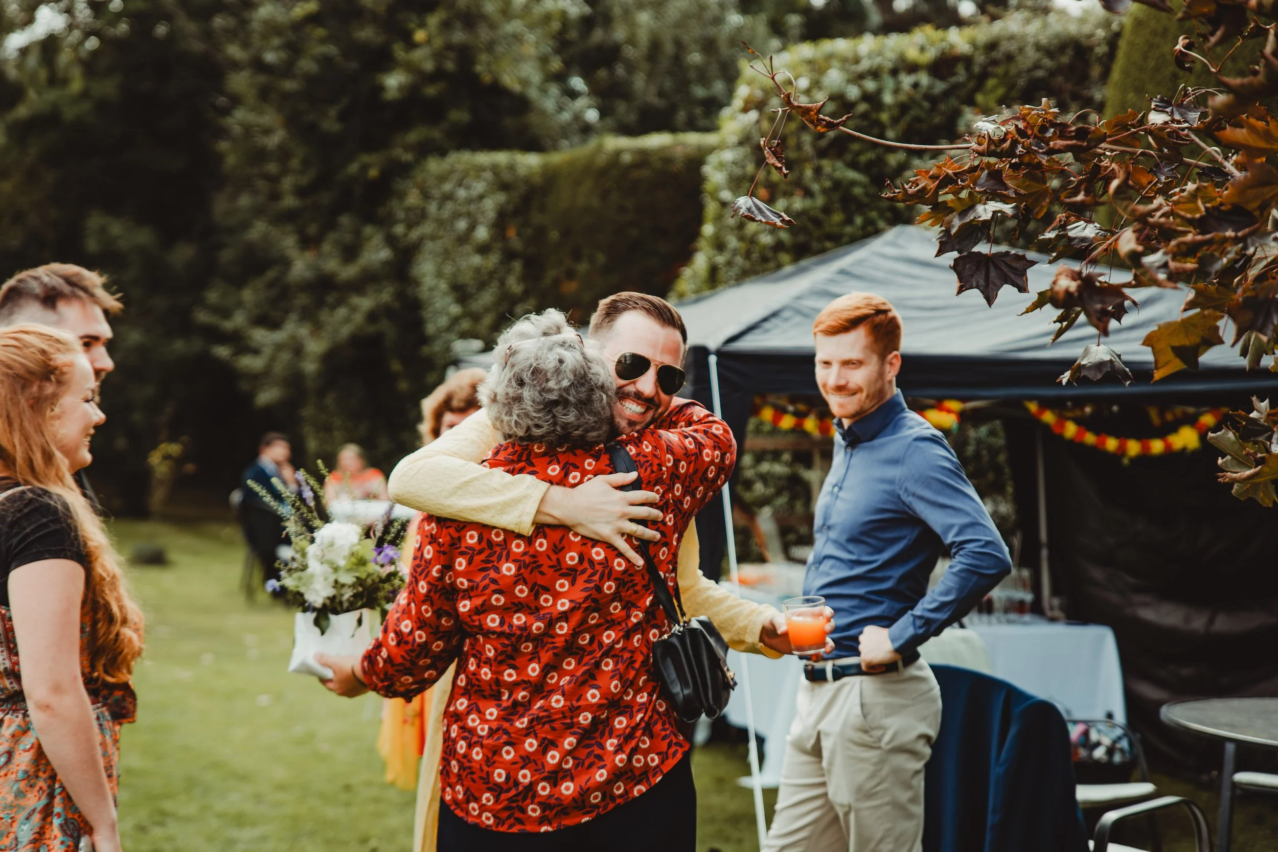 People smiling and hugging at an outdoor gathering with a black canopy, tables, and colorful decorations.