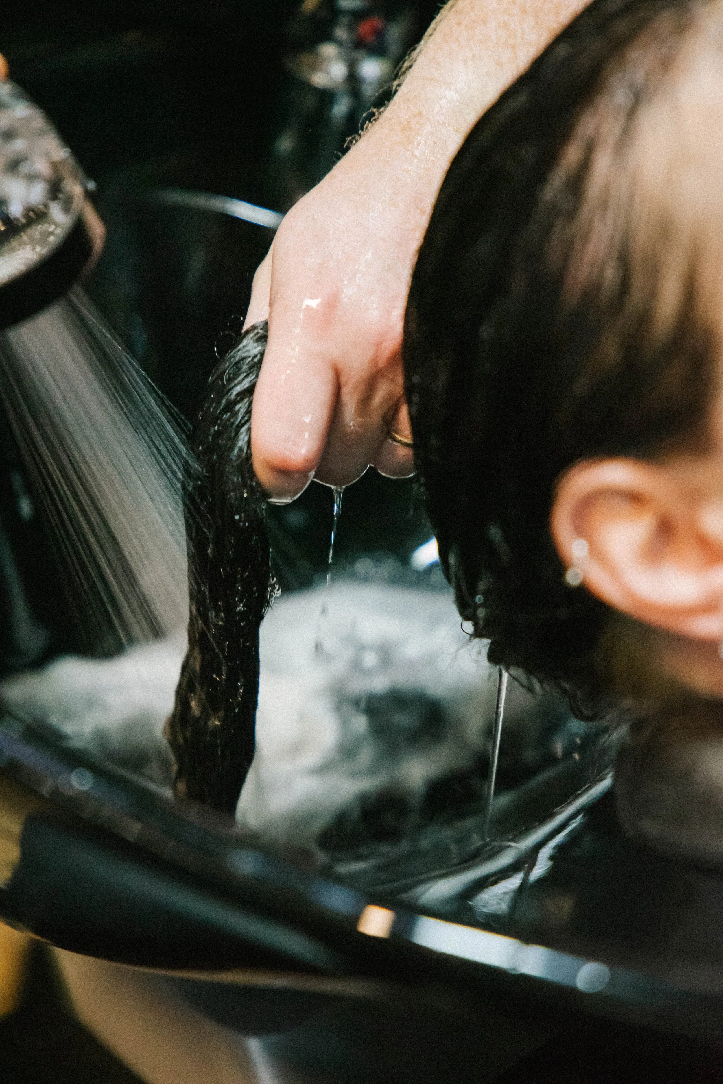A person washing their hair in a sink with water dripping down.