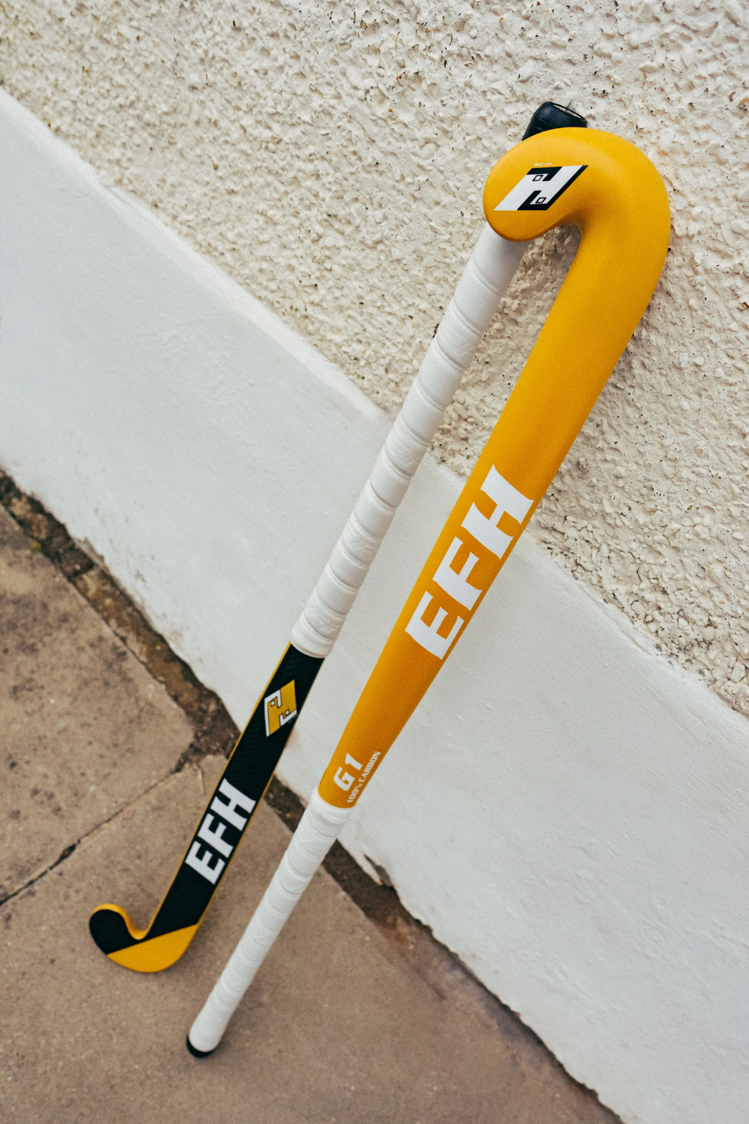 A yellow hockey stick with black and white accents leaning against a white textured wall, the stick has the brand name "EFFECT" printed on it.