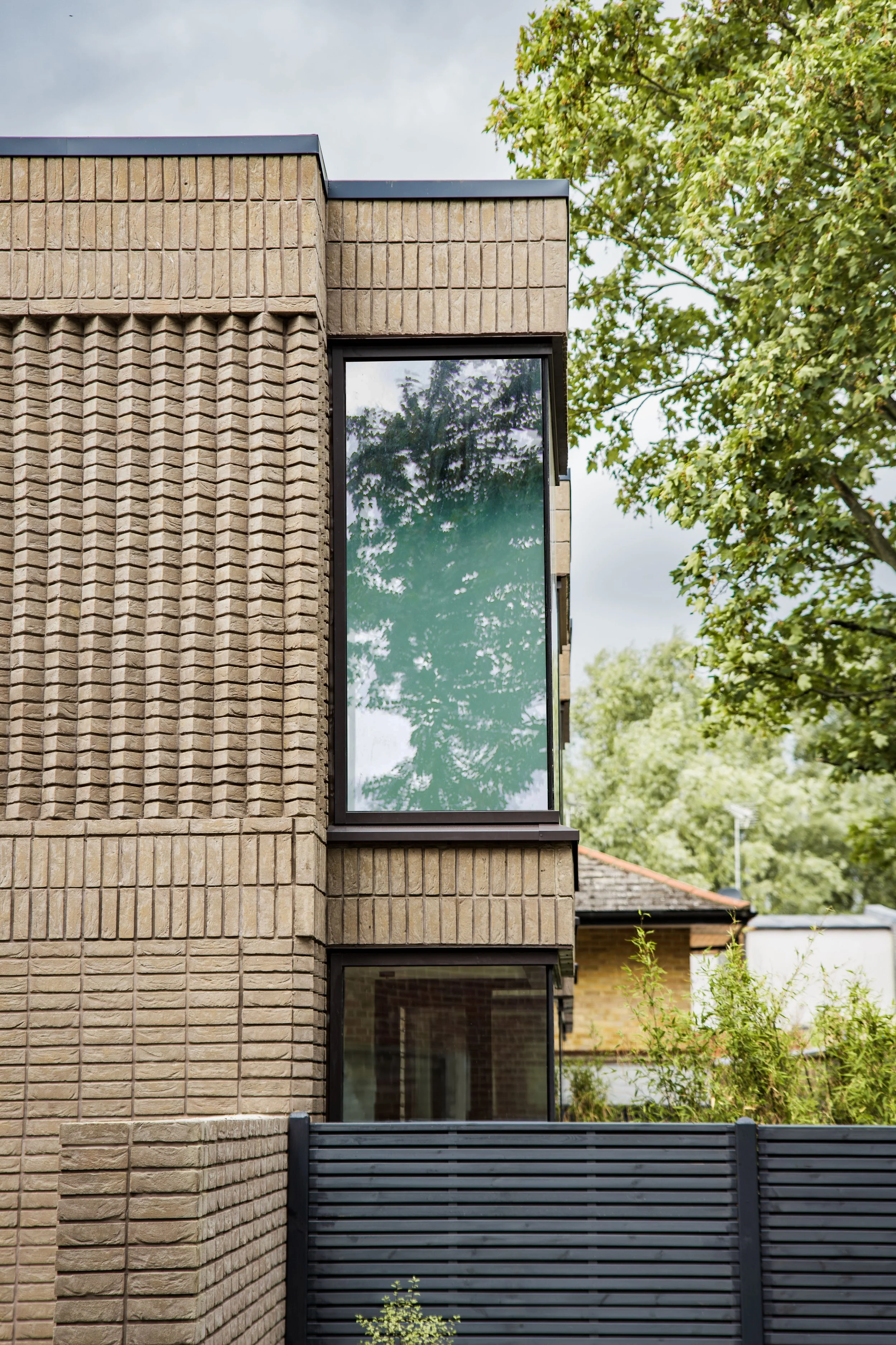 A modern building with a textured brick exterior and large rectangular windows, surrounded by greenery and trees in a suburban neighborhood.
