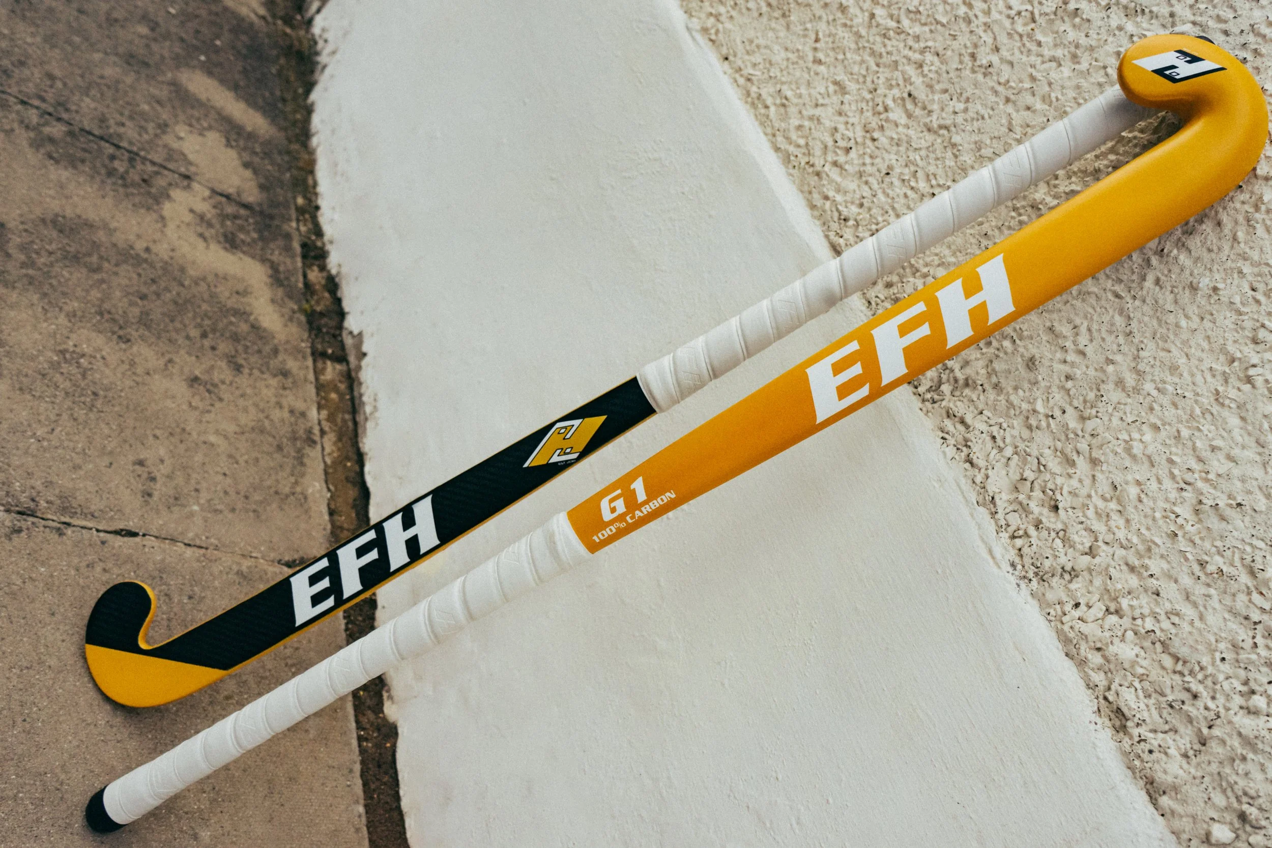 Ice hockey stick with yellow and black design resting against a wall on a speckled floor.