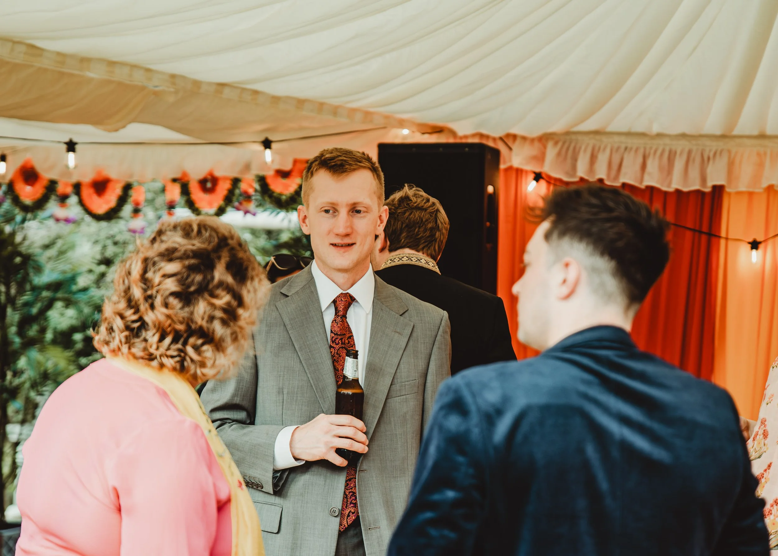 People gathered at an outdoor event under a tent with string lights and red and green decorations.