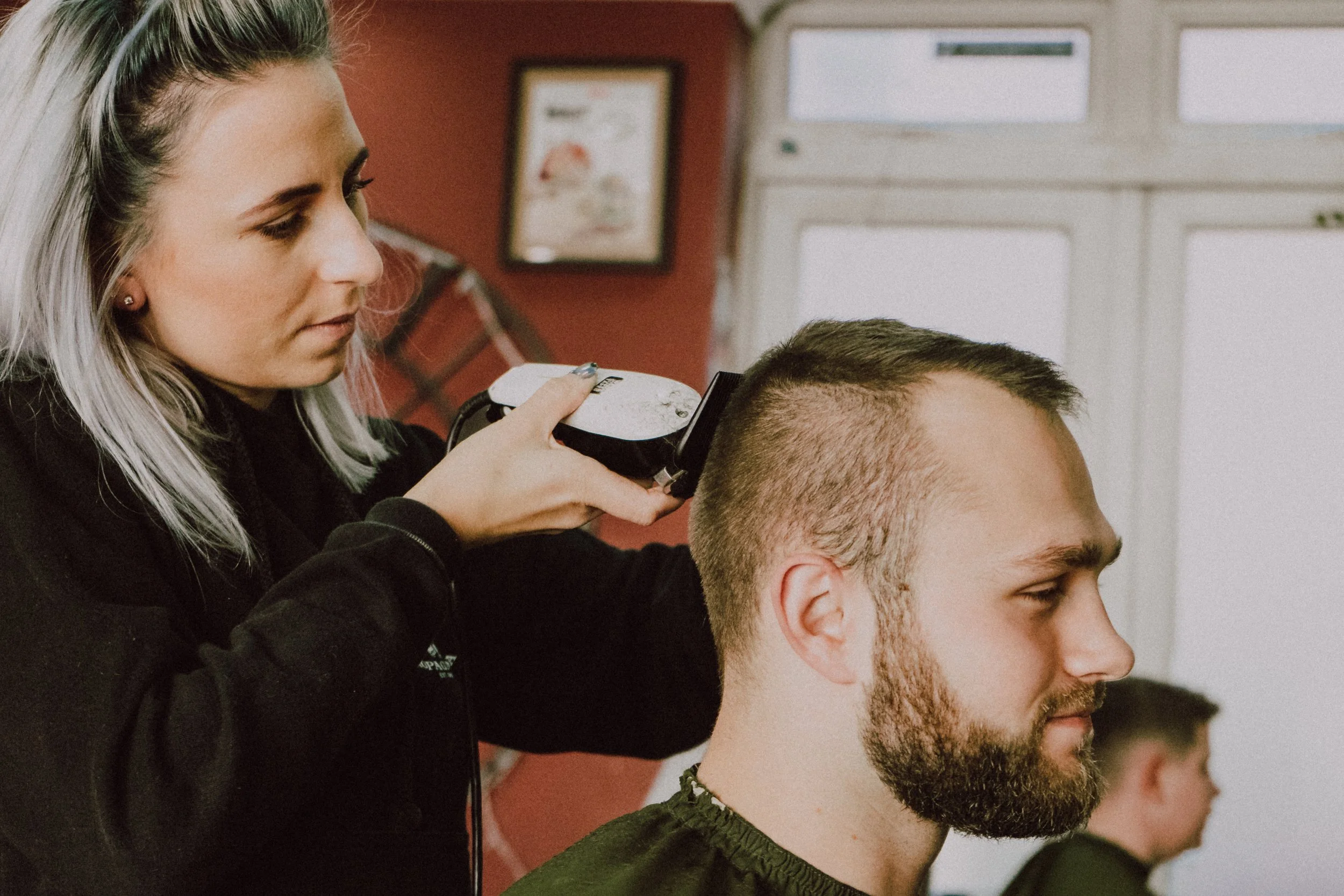 A woman with blonde hair getting a haircut with electric hair clippers from a hairdresser in a salon.