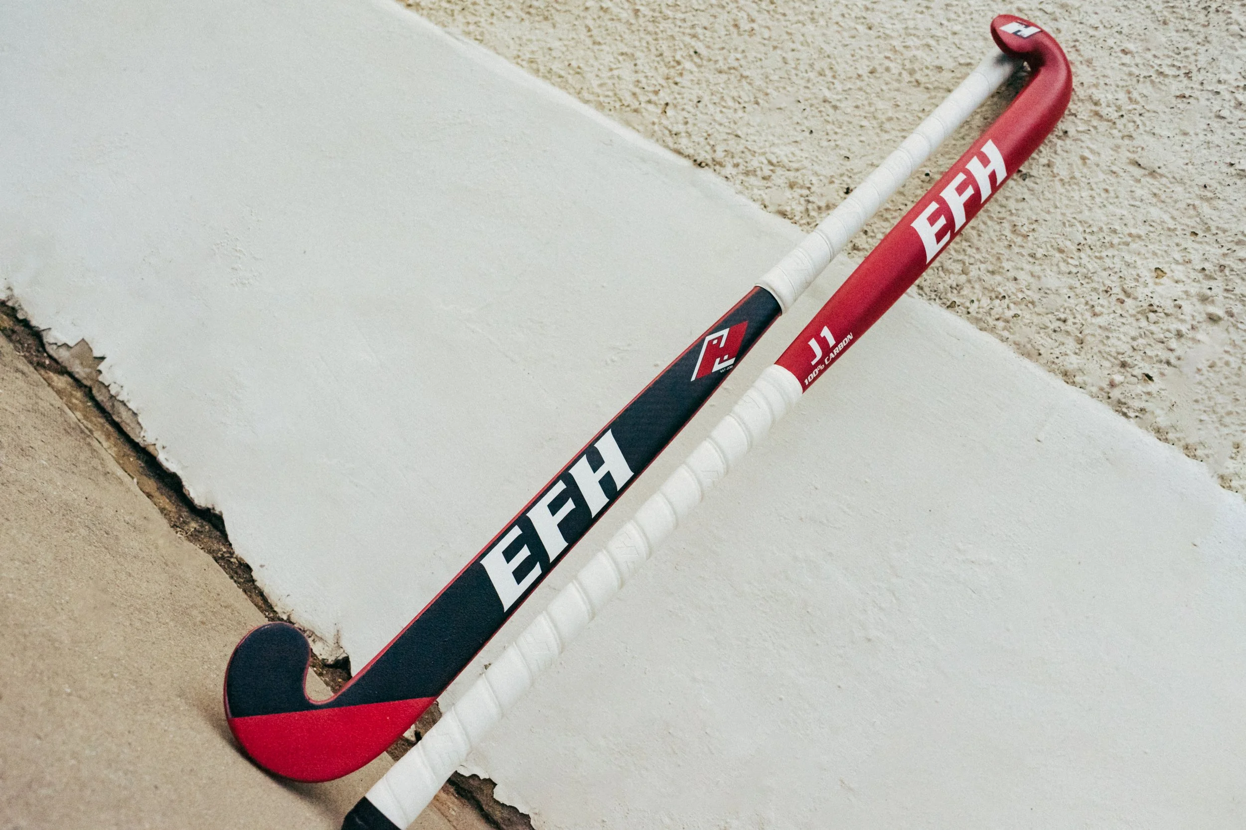 Hockey stick resting against a white wall on a beige textured surface.