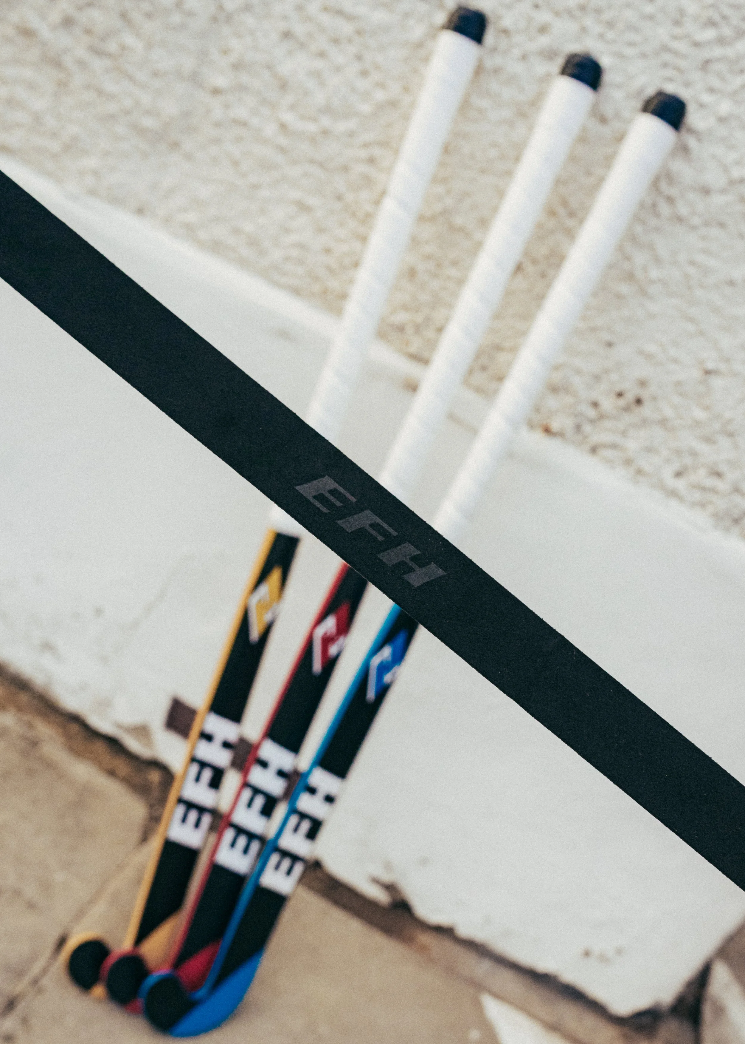 Multiple hockey sticks with colored accents leaning against a white wall.