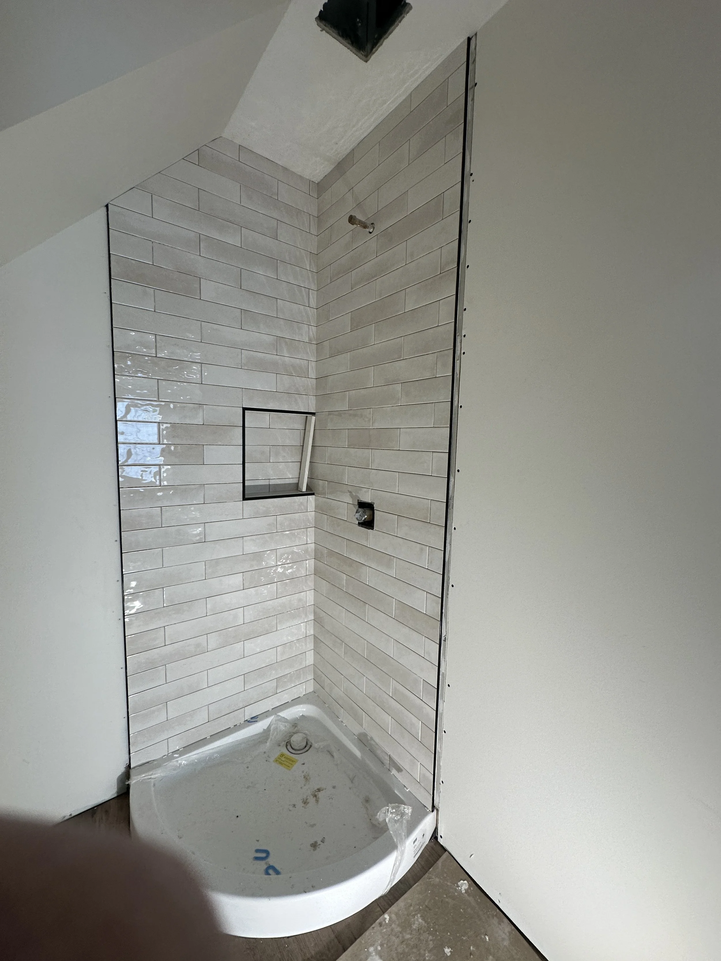 Bathroom shower stall under construction with beige tile walls, black trim, and a plastic shower pan.