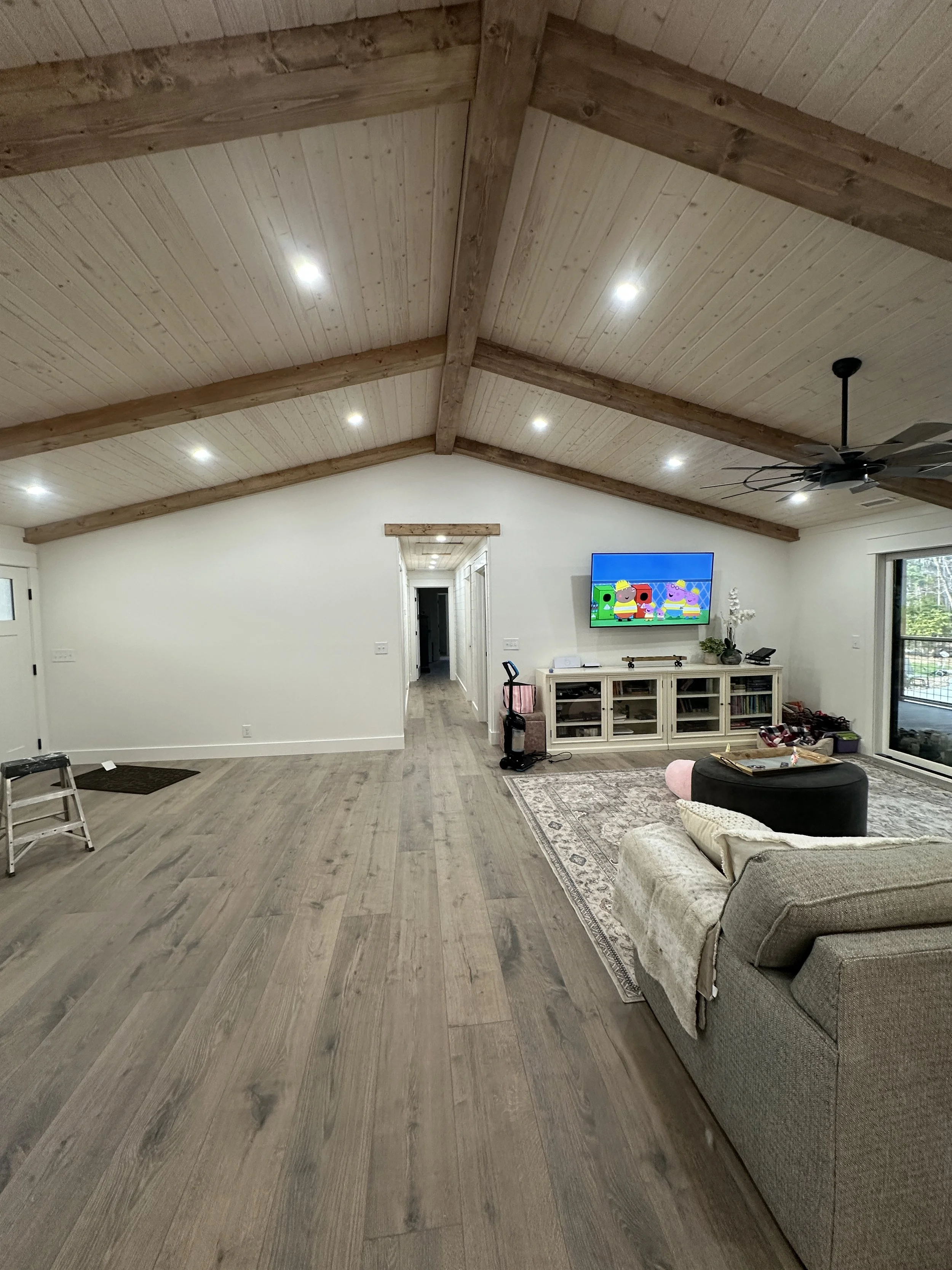 Living room with wood vaulted ceiling, recessed lighting, ceiling fan, gray sofa, TV on stand, sliding glass door, and hallway leading to other rooms.