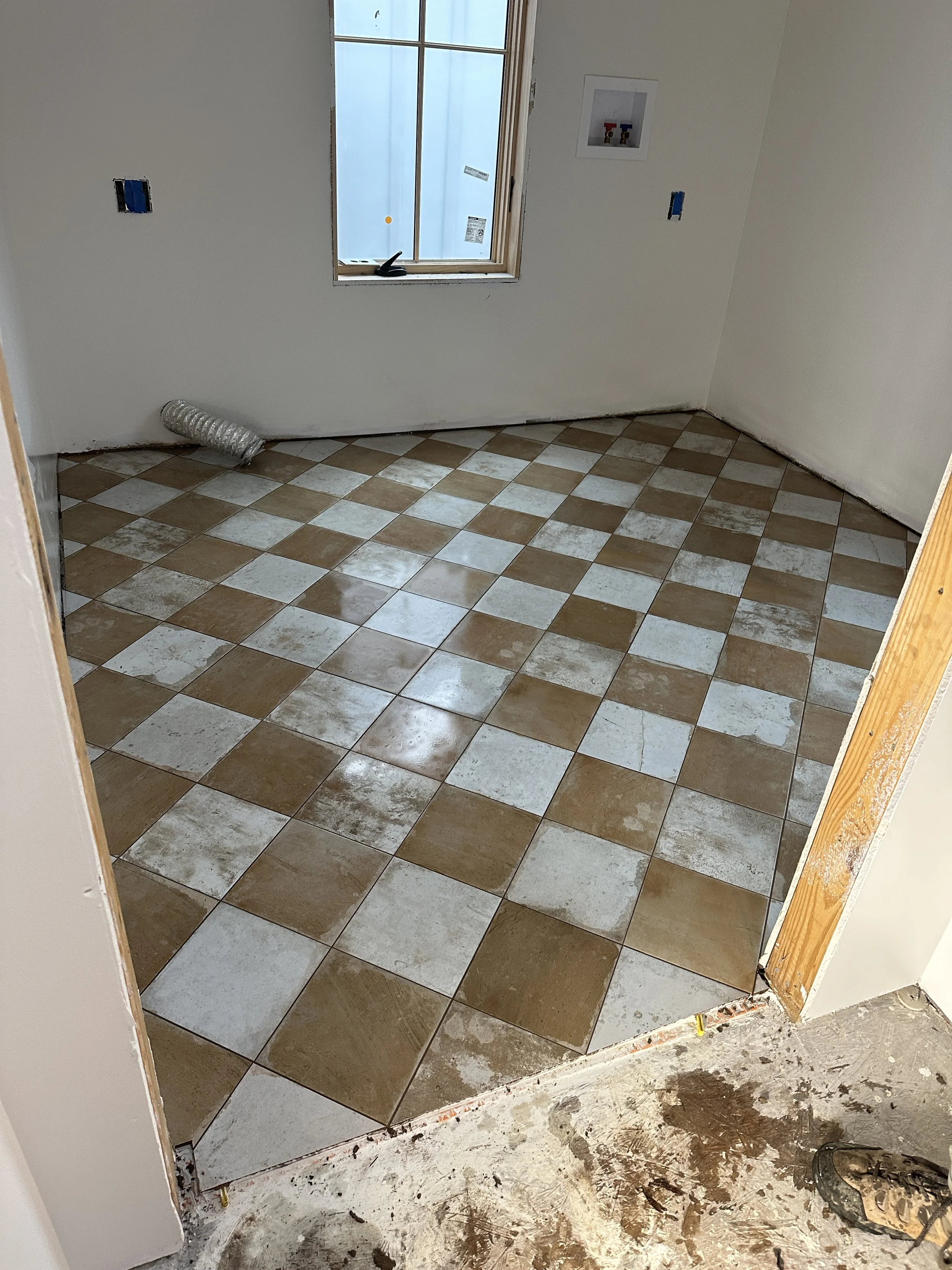 Room under construction with beige and white checkered tile flooring, an unfinished window, and electrical outlets on the wall.