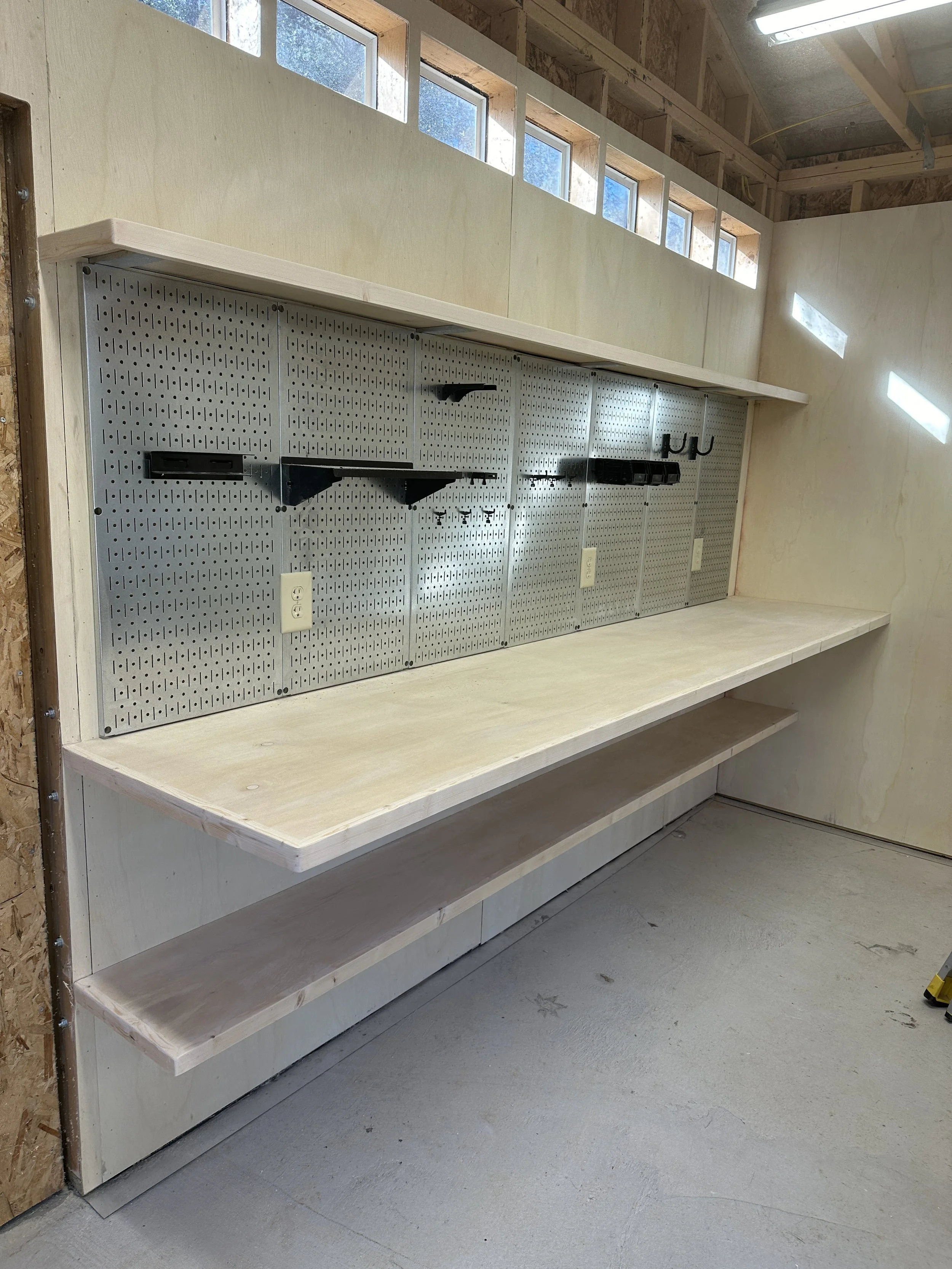 A workbench with a pegboard wall, power outlets, and hooks in a workshop under construction.