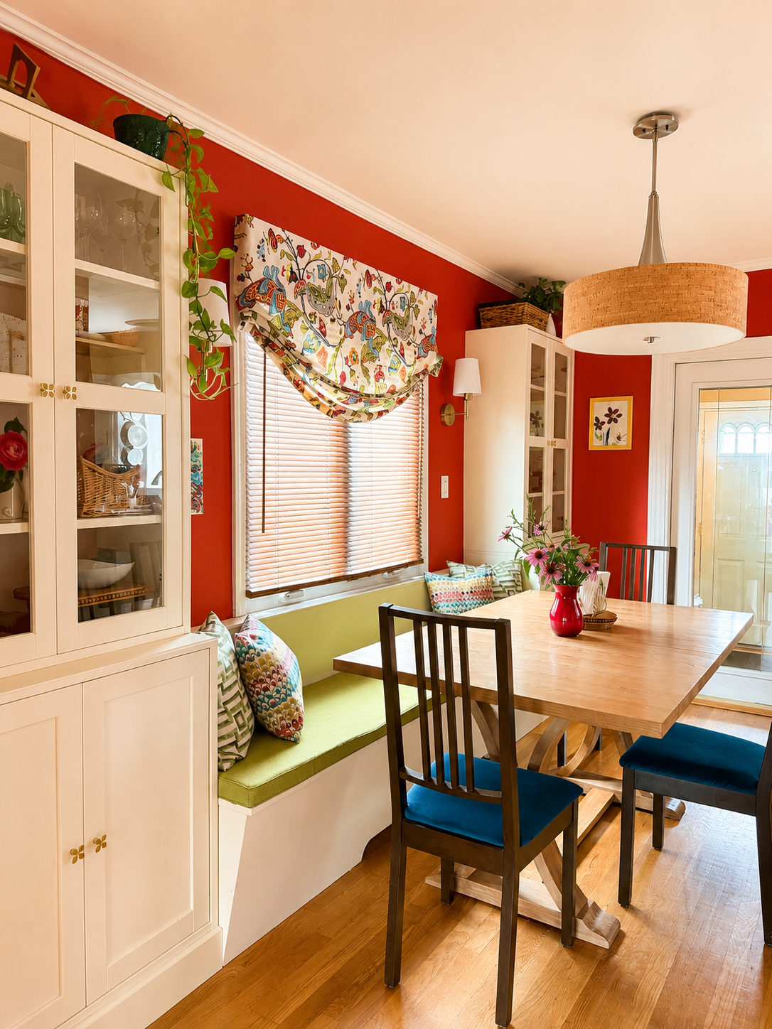 Family dining room redesign featuring custom glass-front storage cabinets, a wooden dining table, colorful floral window treatments, and thoughtful space planning for everyday family living.