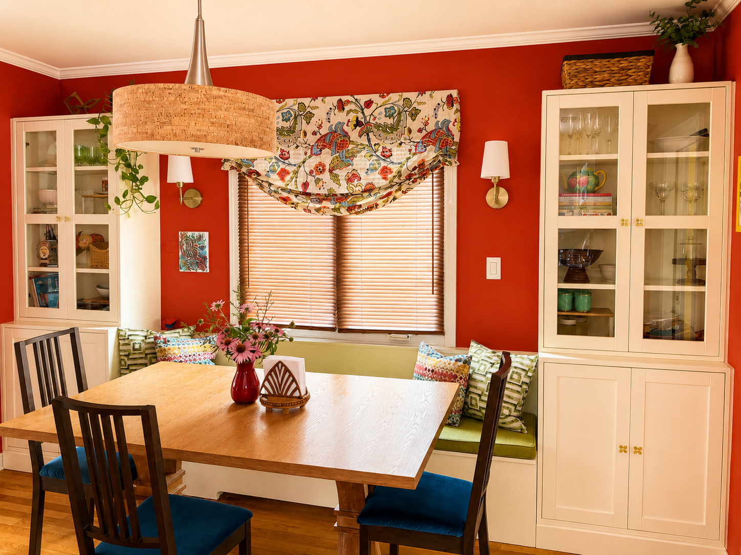 Family dining room redesign featuring custom glass-front storage cabinets, a wooden dining table, colorful floral window treatments, and thoughtful space planning for everyday family living.