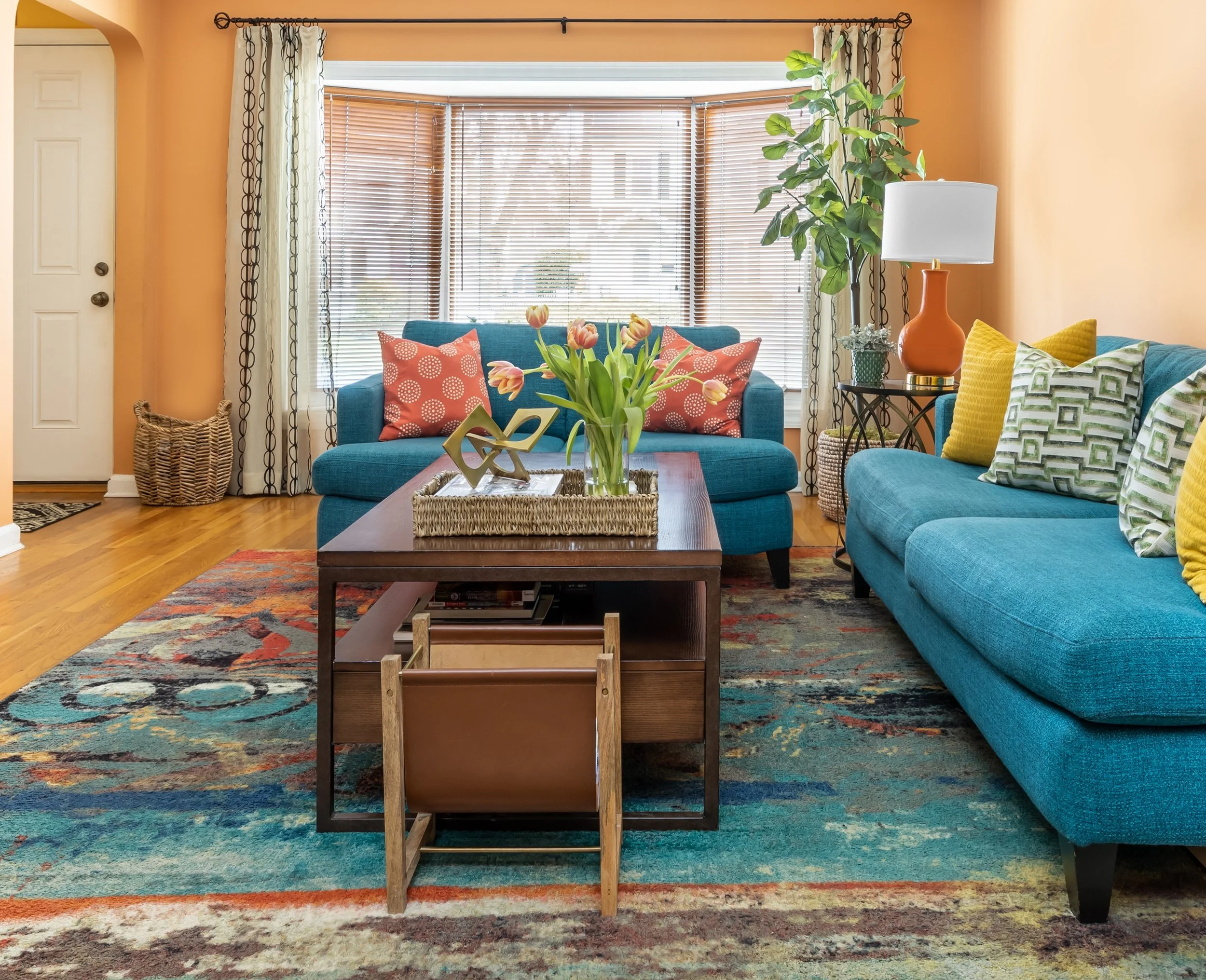 Living room redesign featuring a teal sofa, layered textiles, balanced furniture placement, and a functional layout designed for comfortable family living.