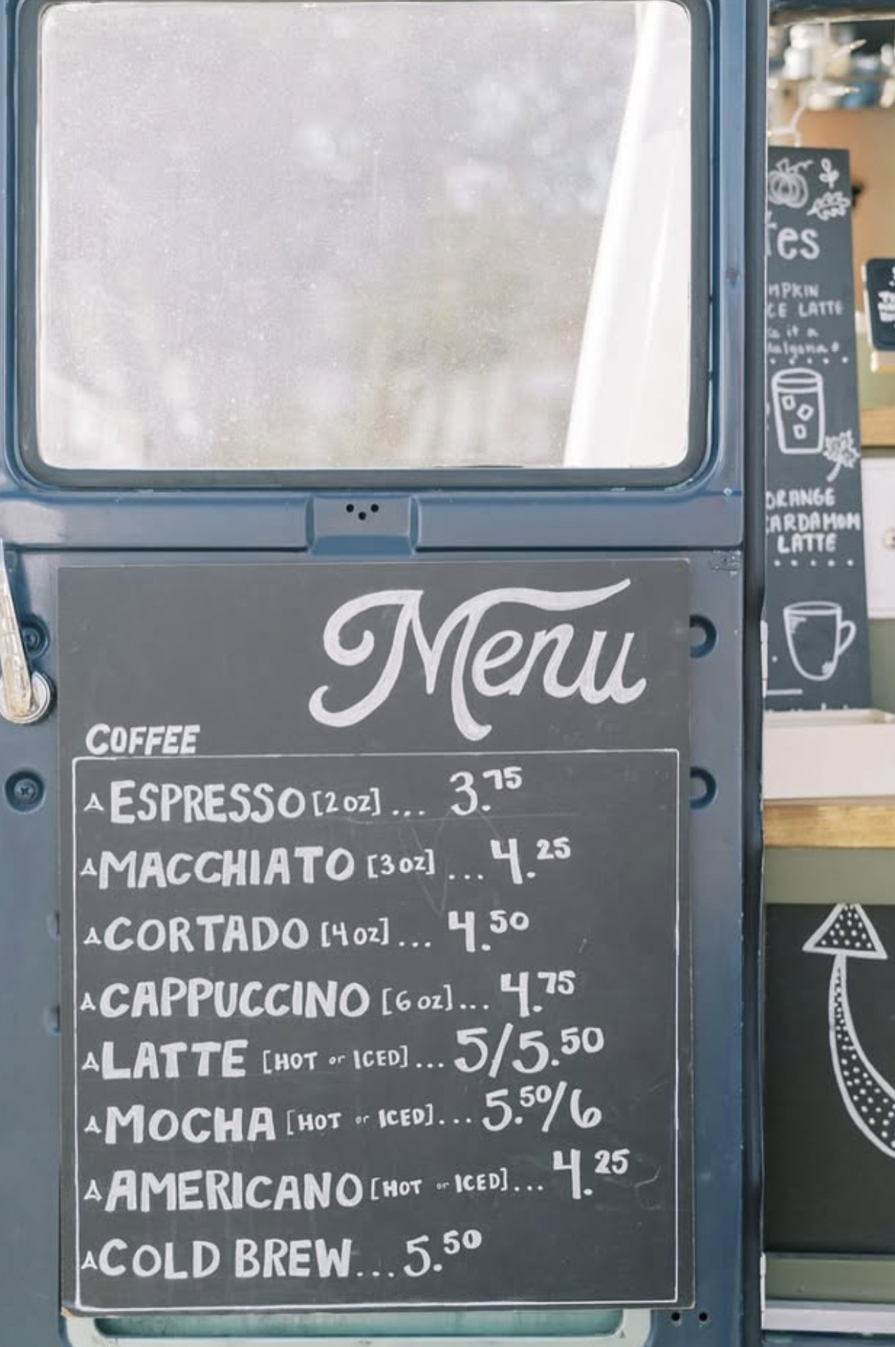 Coffee menu board listing various espresso drinks with prices, including espresso, macchiato, cortado, cappuccino, latte, mocha, americano, and cold brew.
