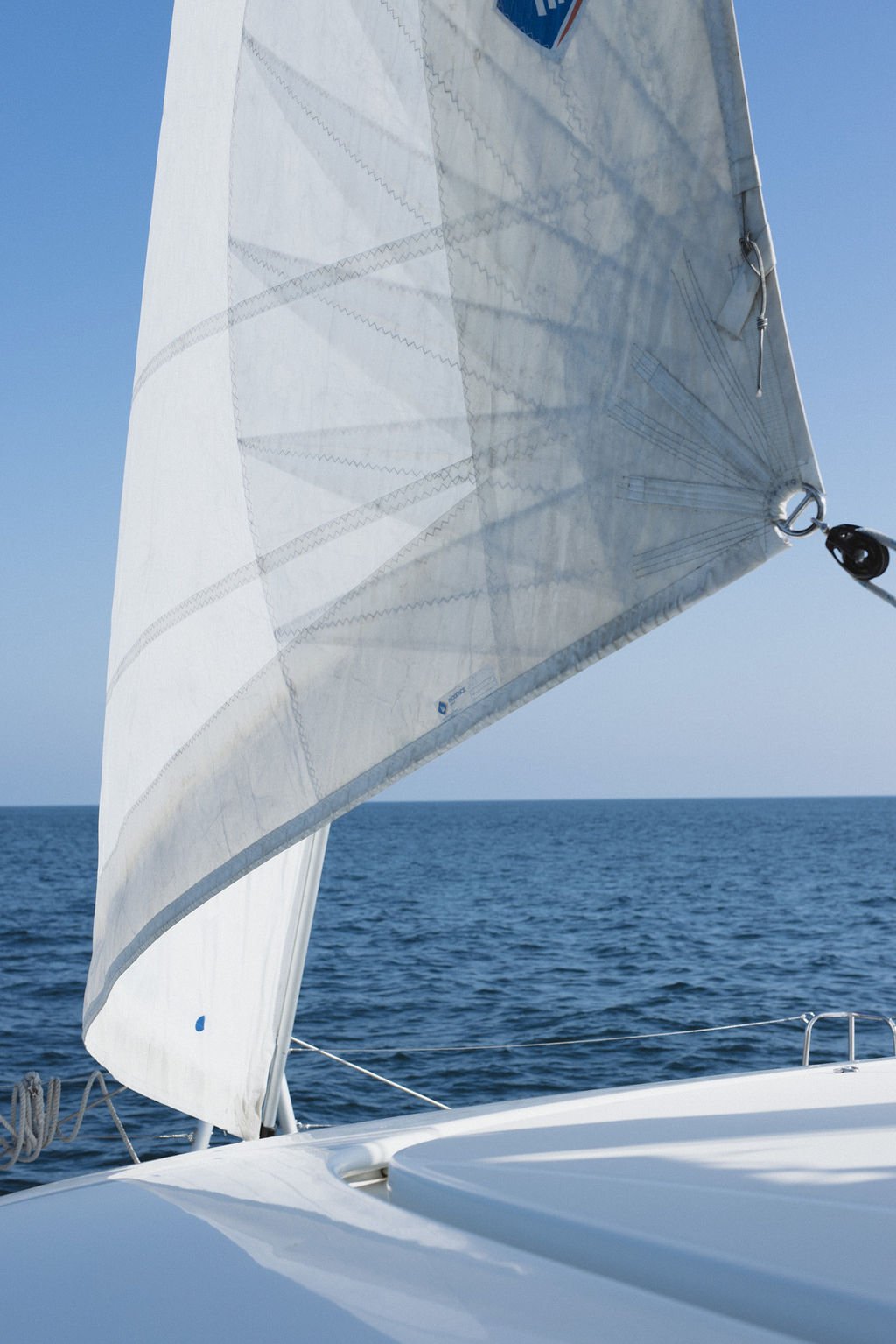 Close-up of a white sailboat sail on the open ocean on a sunny day.
