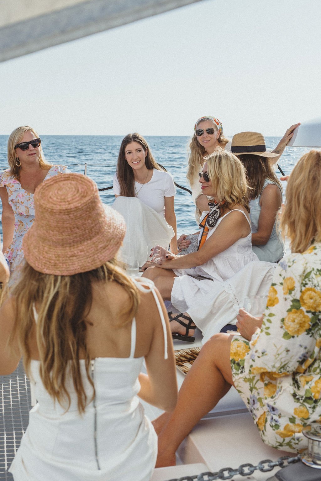 Group of women enjoying a boat ride on the ocean, some wearing hats and sunglasses, engaged in conversation and smiling.
