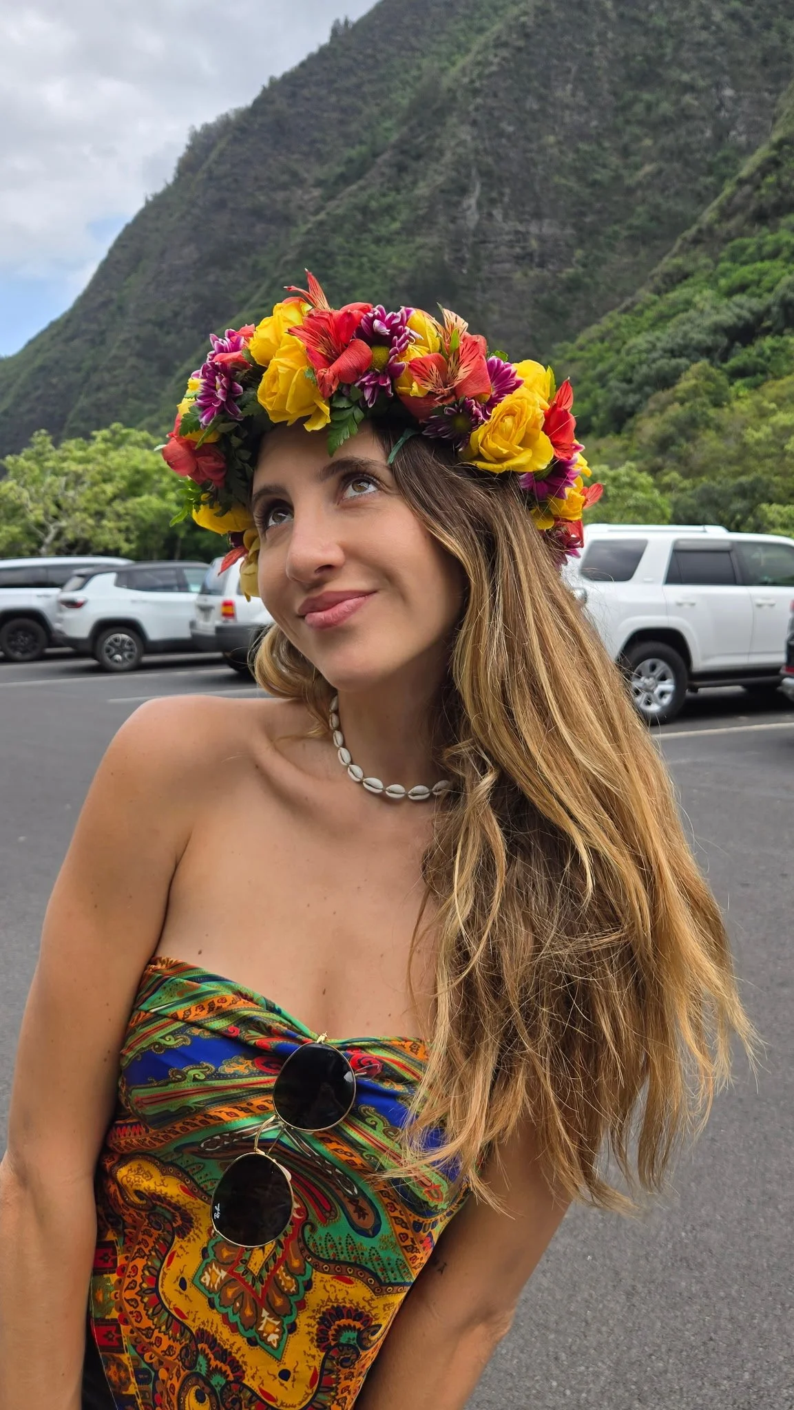 A smiling woman with long wavy hair wearing a pink hat and black sunglasses, standing outdoors near a boat with other women in the background.