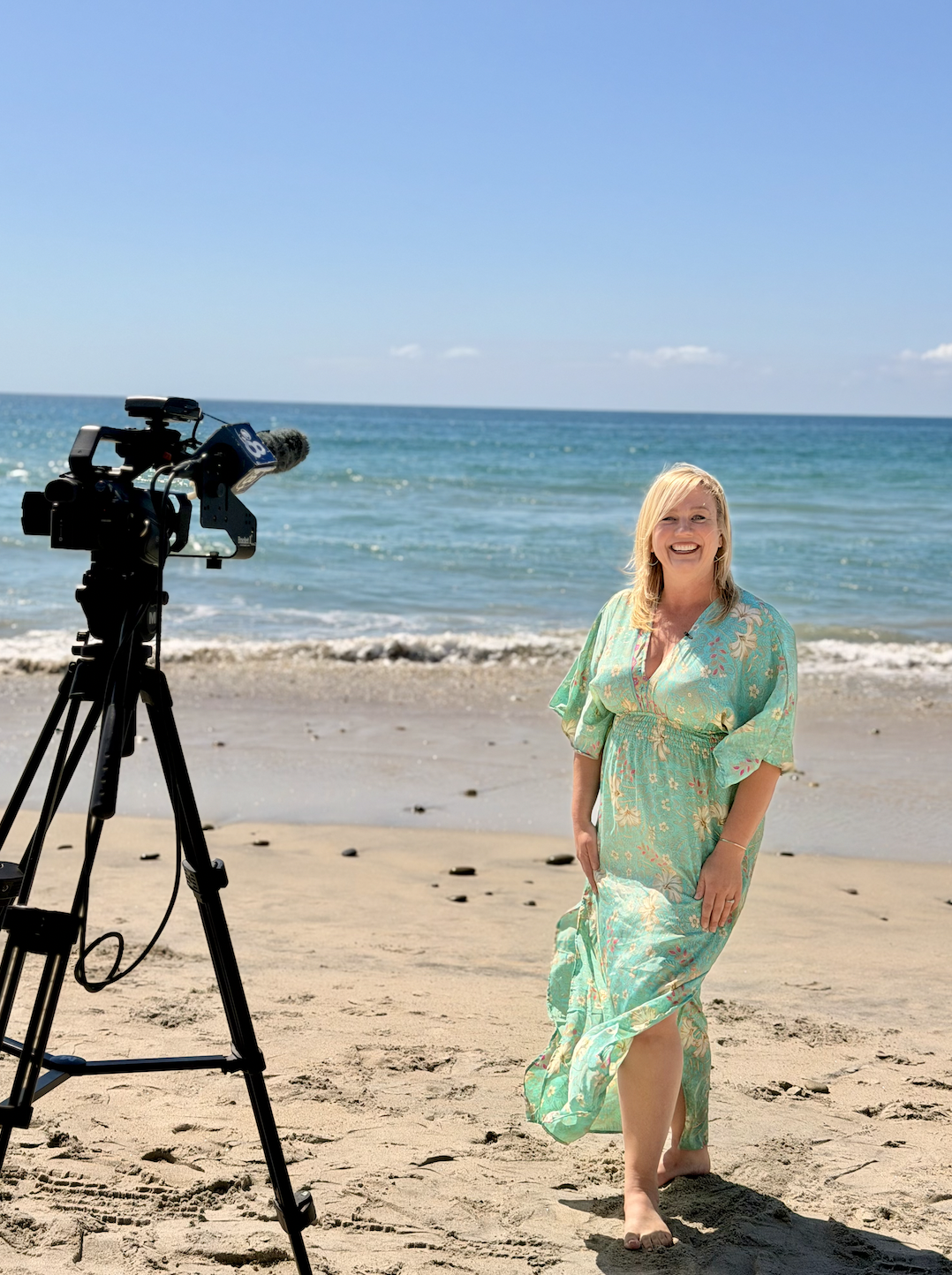 Smiling woman on the beach wearing a light blue cap and a grey t-shirt with 'DESTIN Florida' written on it.