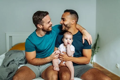 Two fathers smiling with their young child while spending quality time together at home, representing diverse families, positive parenting, early childhood development, and family connection.