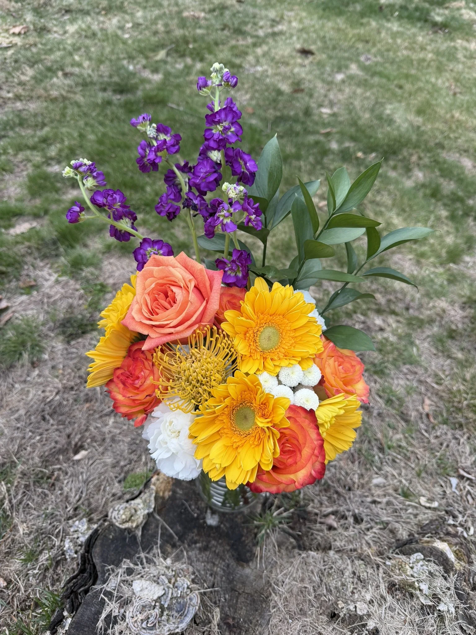 Colorful bouquet of flowers with purple, orange, yellow, and white blooms on a grassy background.