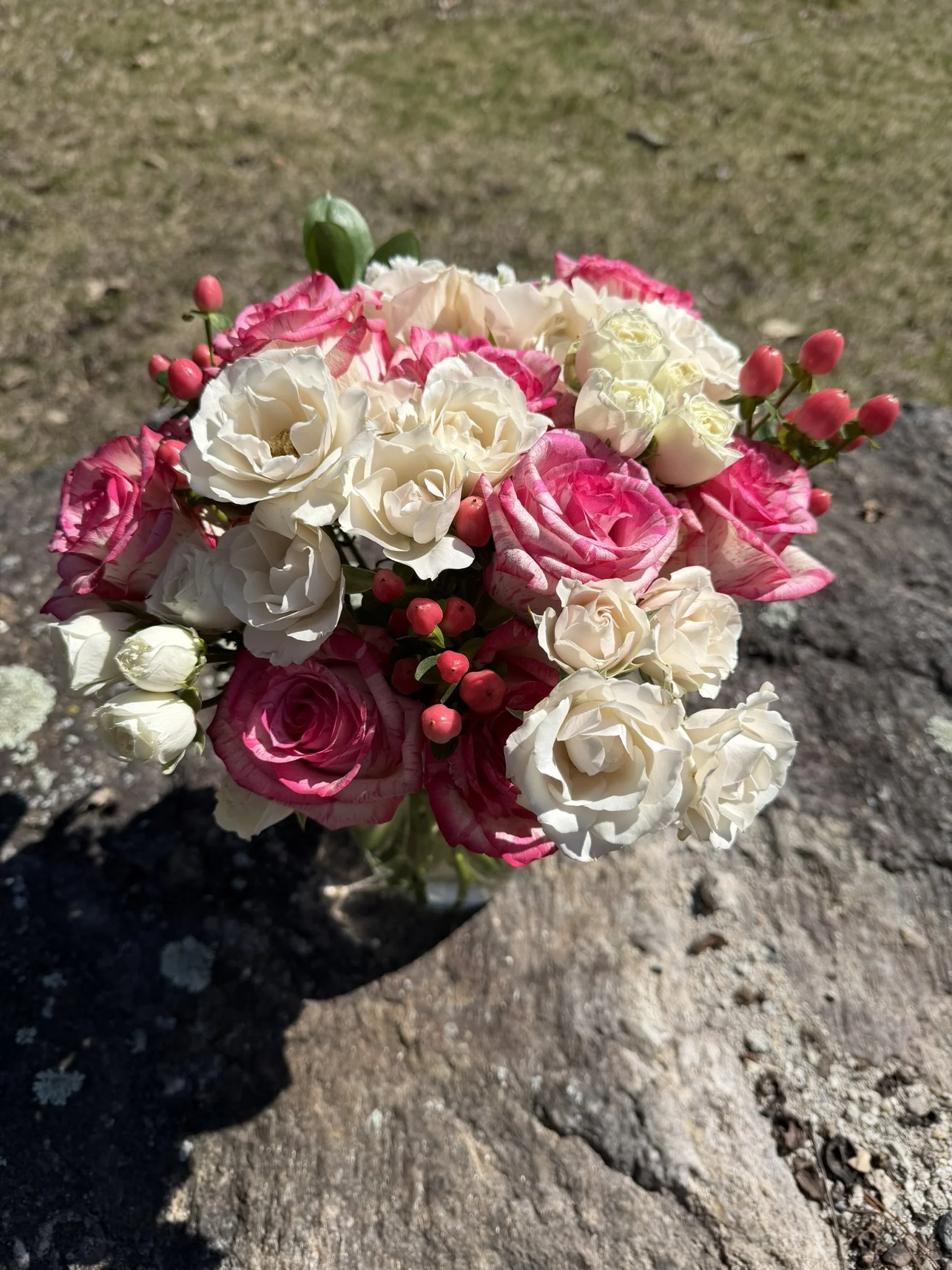 A bouquet of mixed white and pink flowers resting on a dirt ground, with the shadow of the bouquet cast on the soil.