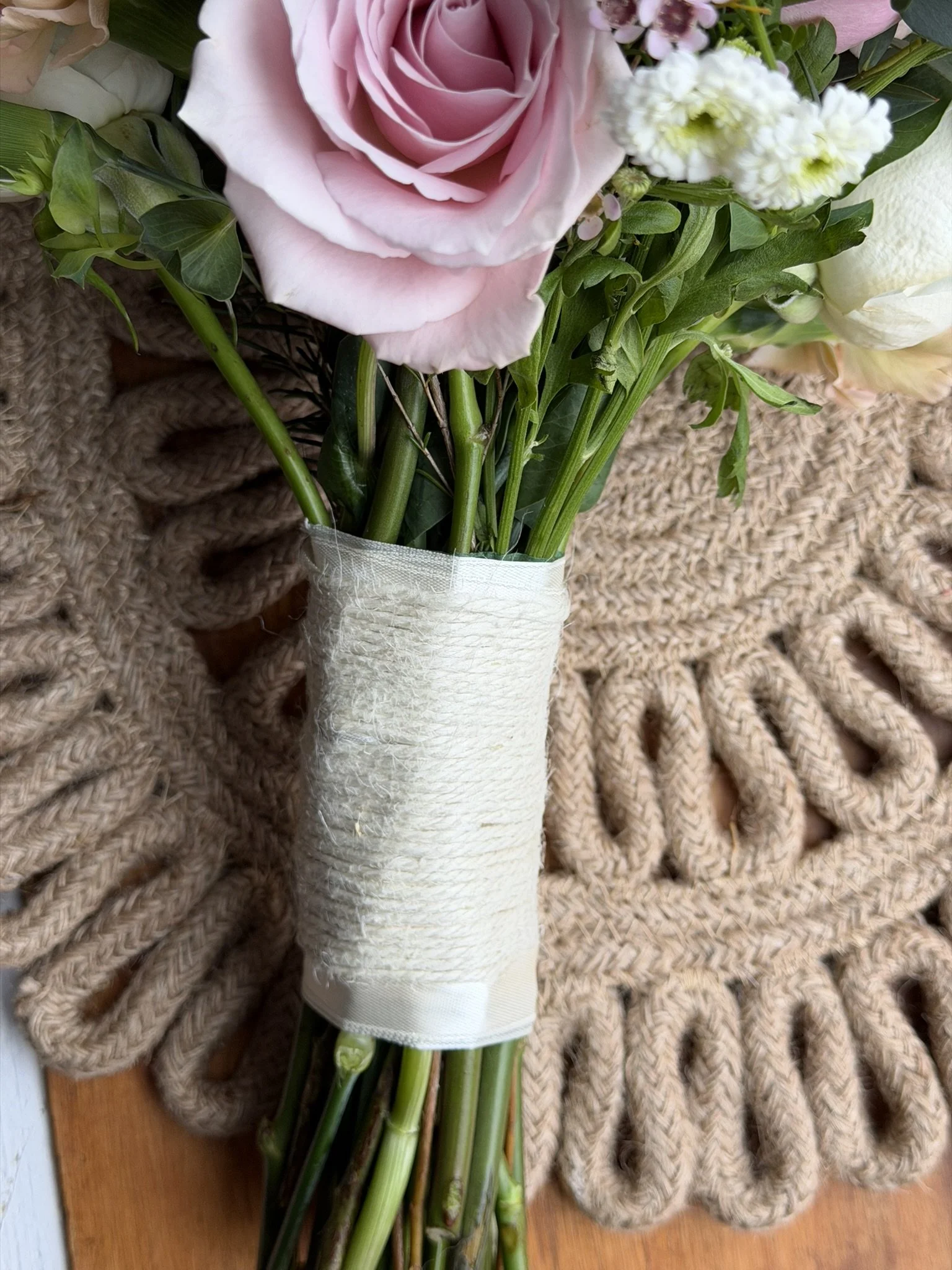 A bouquet of pink roses, white flowers, and greenery wrapped with white ribbon placed on a textured beige blanket.