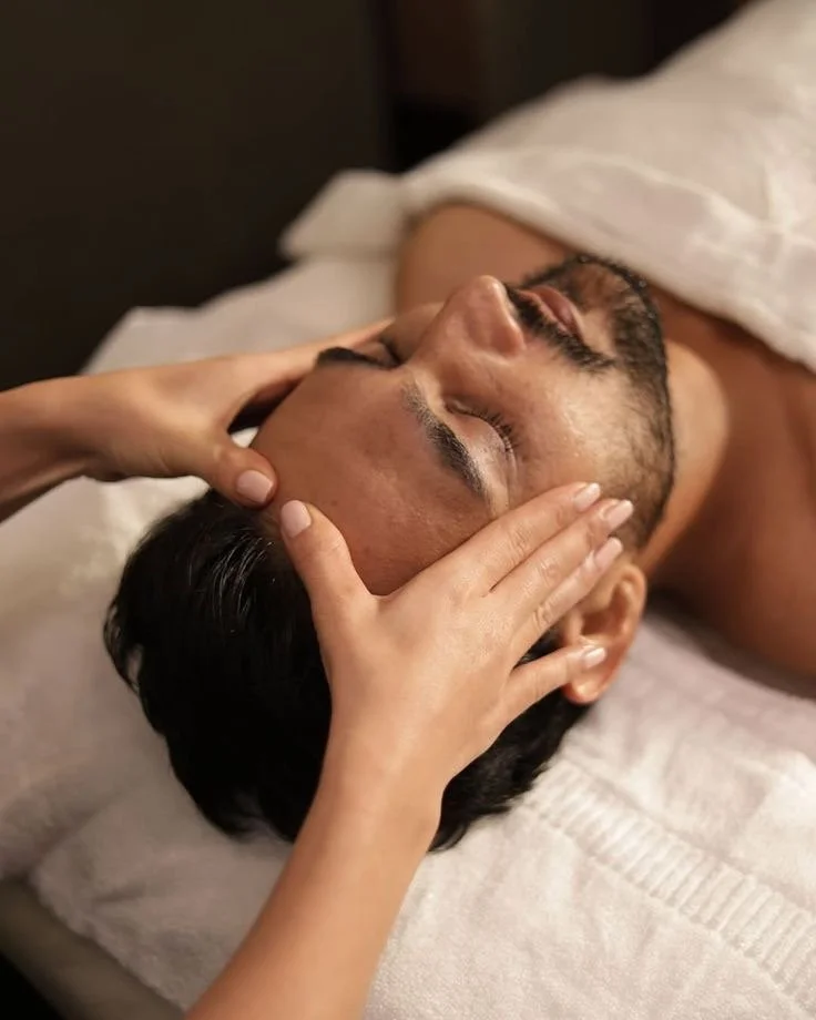 Una persona recibiendo un masaje facial en una cama con una toalla blanca.
