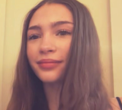 A young woman with long brown hair and light skin smiling at the camera.