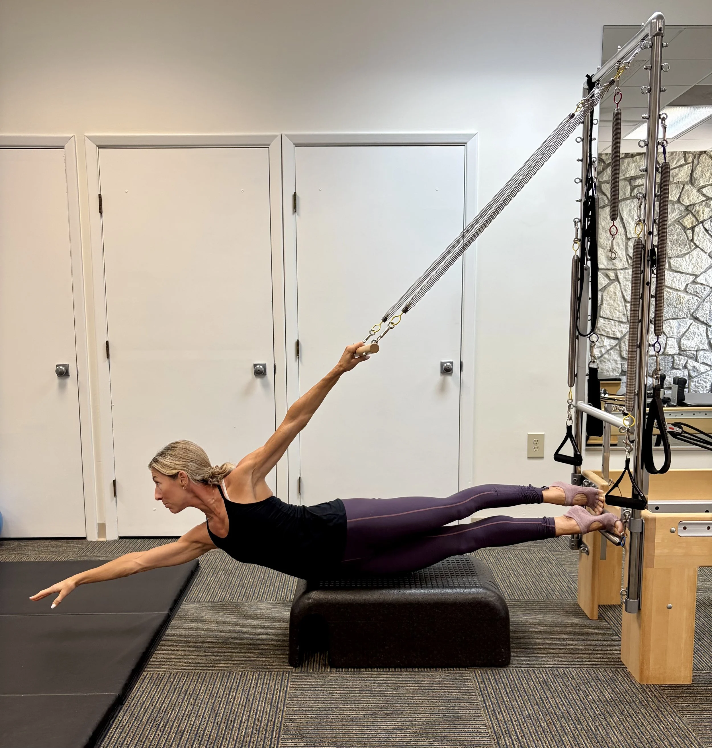 Woman doing a yoga pose on a Pilates reformer machine in a fitness studio, with a focus on stretching and balance.