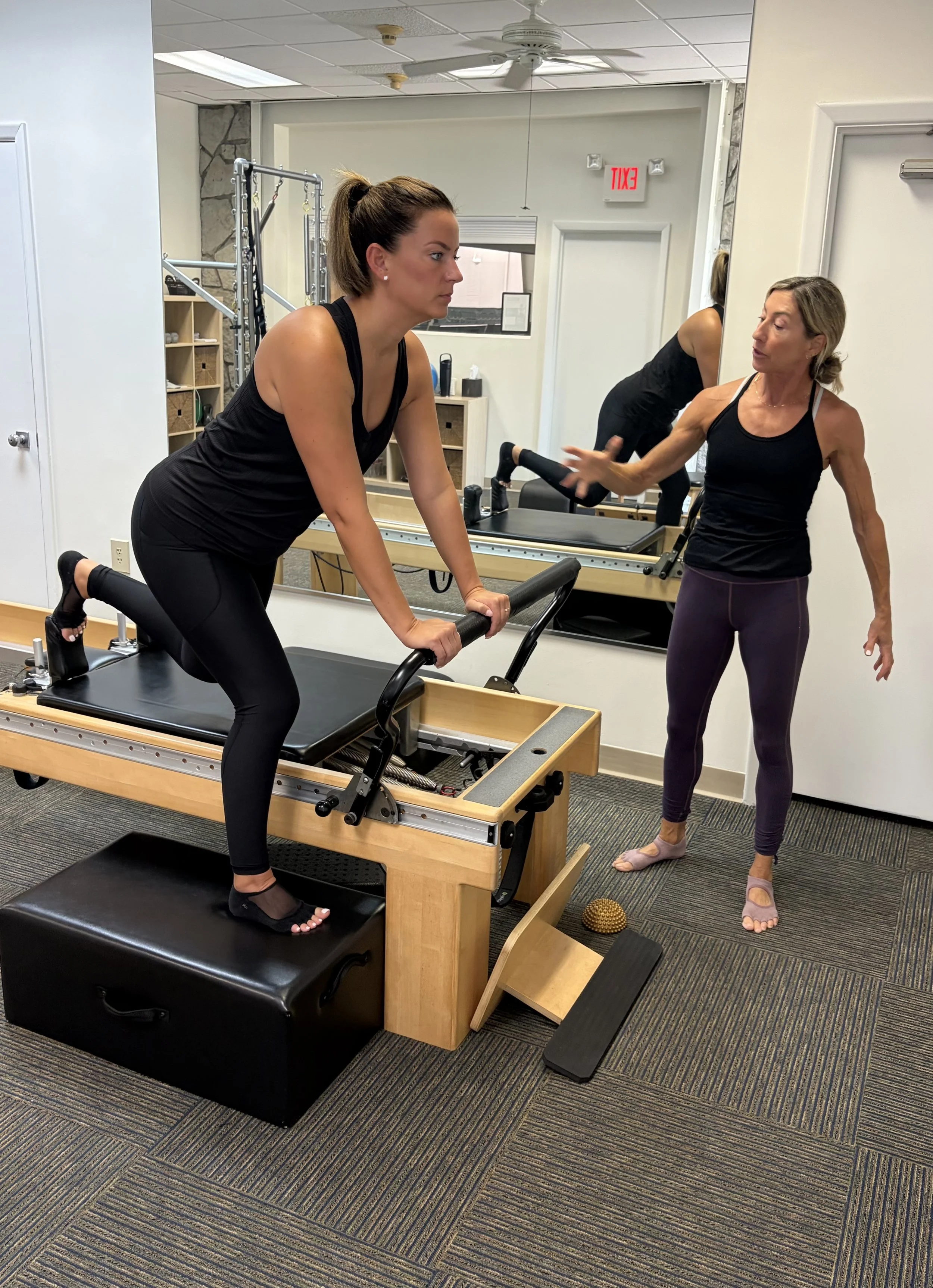 A woman is doing a Pilates exercise on a reformer machine while an instructor provides guidance in a fitness studio.