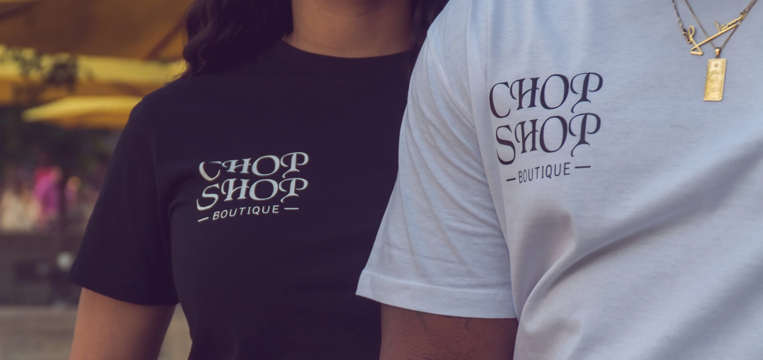 Close-up of two people wearing t-shirts with 'Chop Shop Boutique' logos, one in black and one in white.
