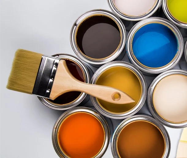Barattoli di vernice di vari colori su sfondo bianco, con un pennello appoggiato sopra