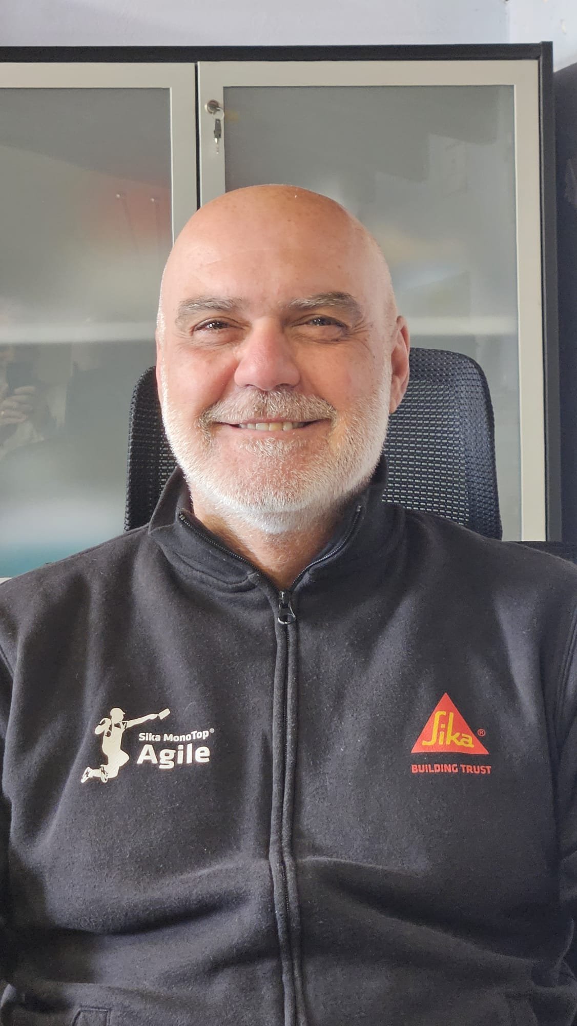 Peppe Portuesi, responsabile vendite, indossa una giacca nera con loghi di Sika MonoTop Agile e Sika Building Trust, sorridente