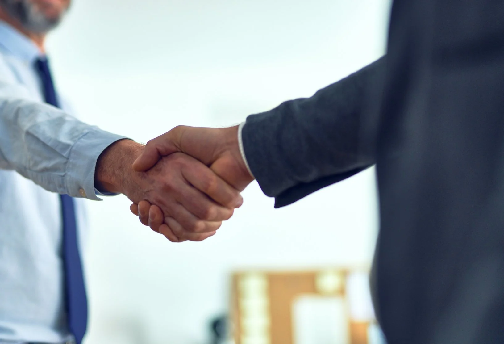 Due uomini si stringono la mano durante un incontro d'affari, entrambi indossano abiti formali.